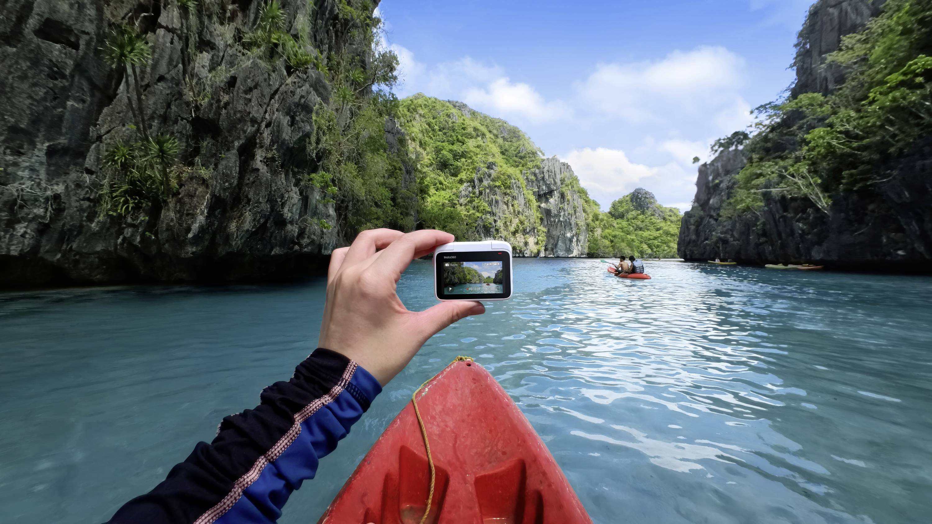 Una persona in kayak tiene in mano una fotocamera e scatta una foto di un paesaggio fluviale pittoresco, con ripide pareti rocciose e acque cristalline.