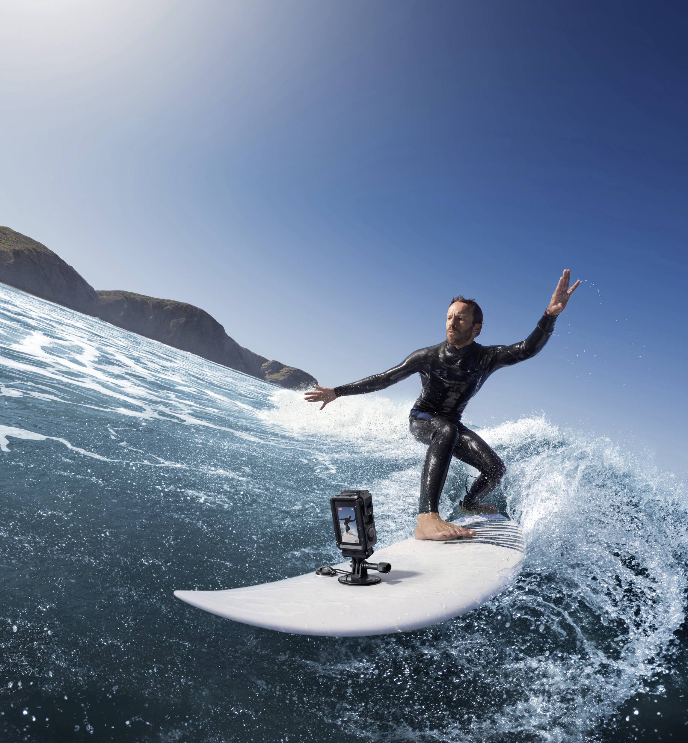 Un uomo fa surf su un'onda, alzando la mano destra a formare il segno della pace. La telecamera sul surf board riprende l'azione.