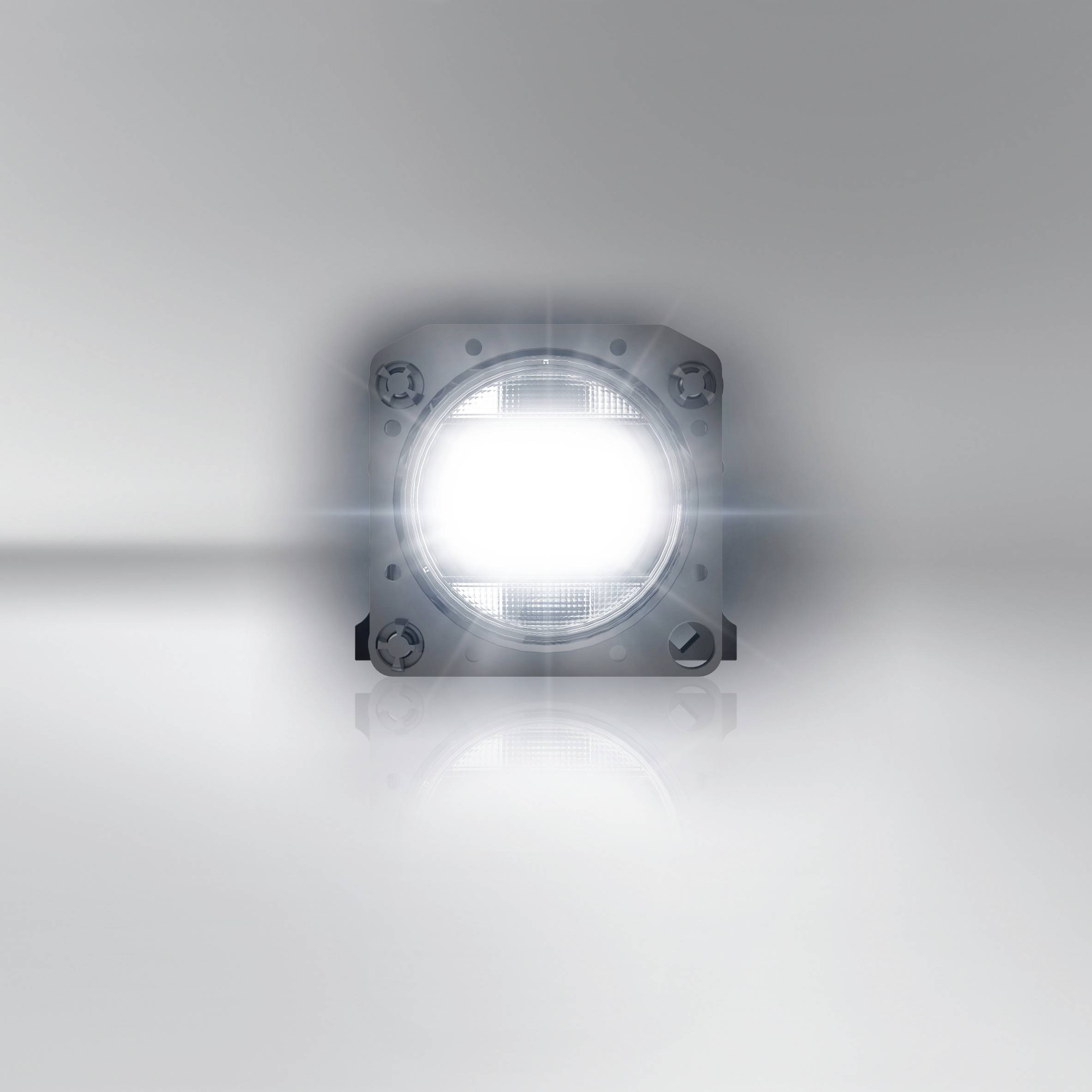 Lampada LED su un tavolo riflettente, che risplende in una luce bianca intensa, circondato da uno sfondo grigio minimalista.