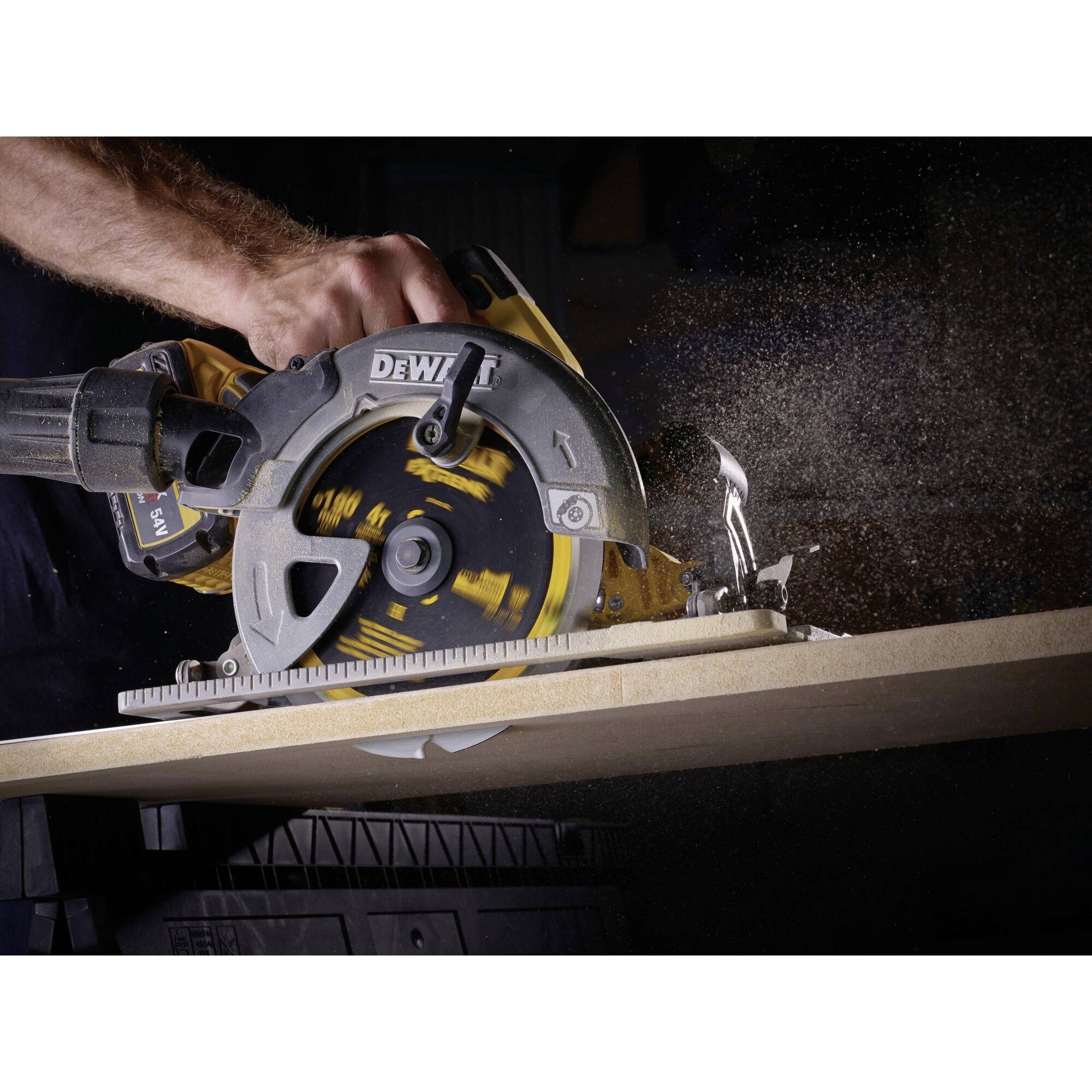 Una sega circolare taglia una tavola di legno. La sega è tenuta da una persona, trucioli di legno volano nell'aria.