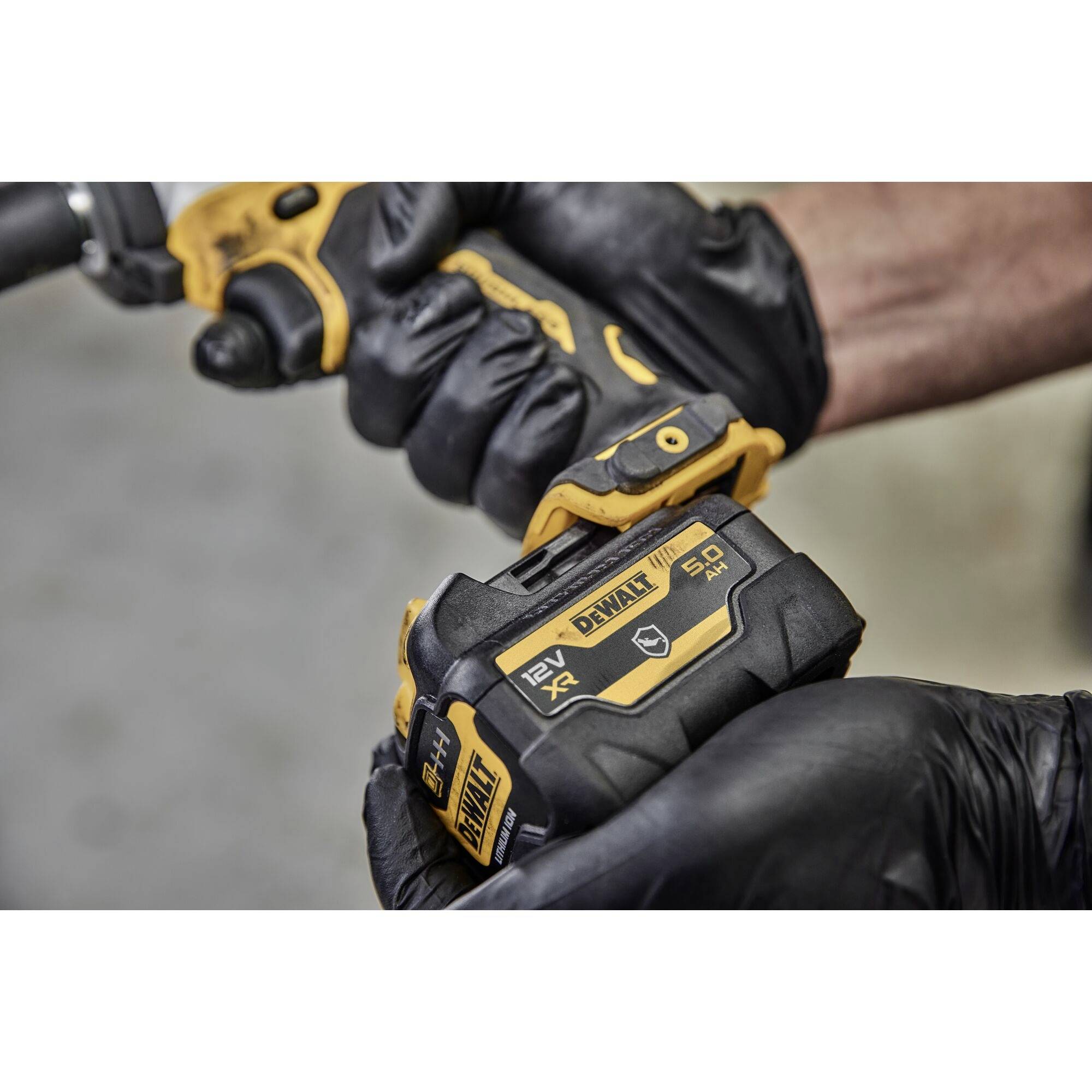 Una persona tiene un trapano elettrico giallo con una batteria da 12V 5.0Ah. Indossa guanti neri.