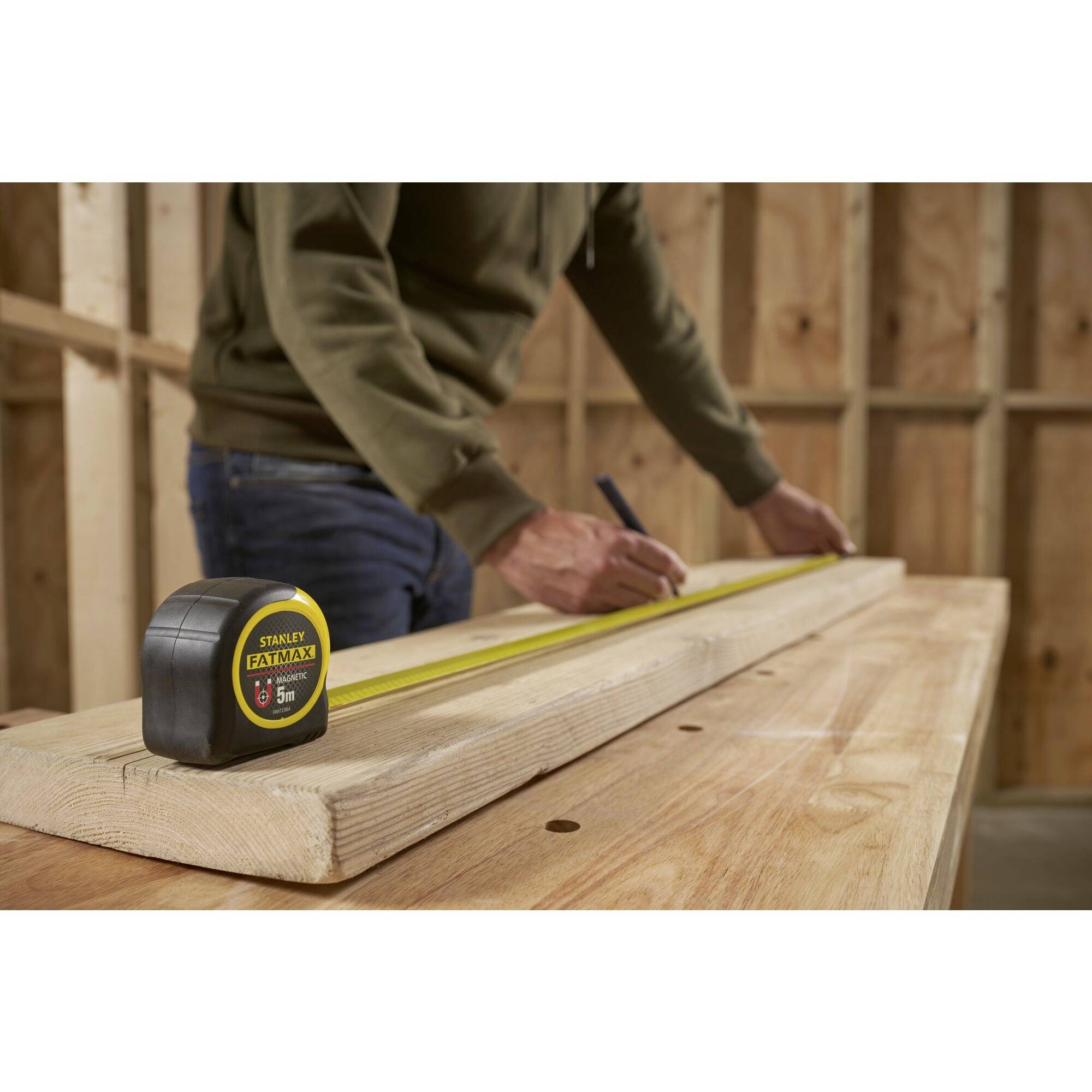 Una persona misura una tavola di legno con un metro a nastro in un laboratorio.