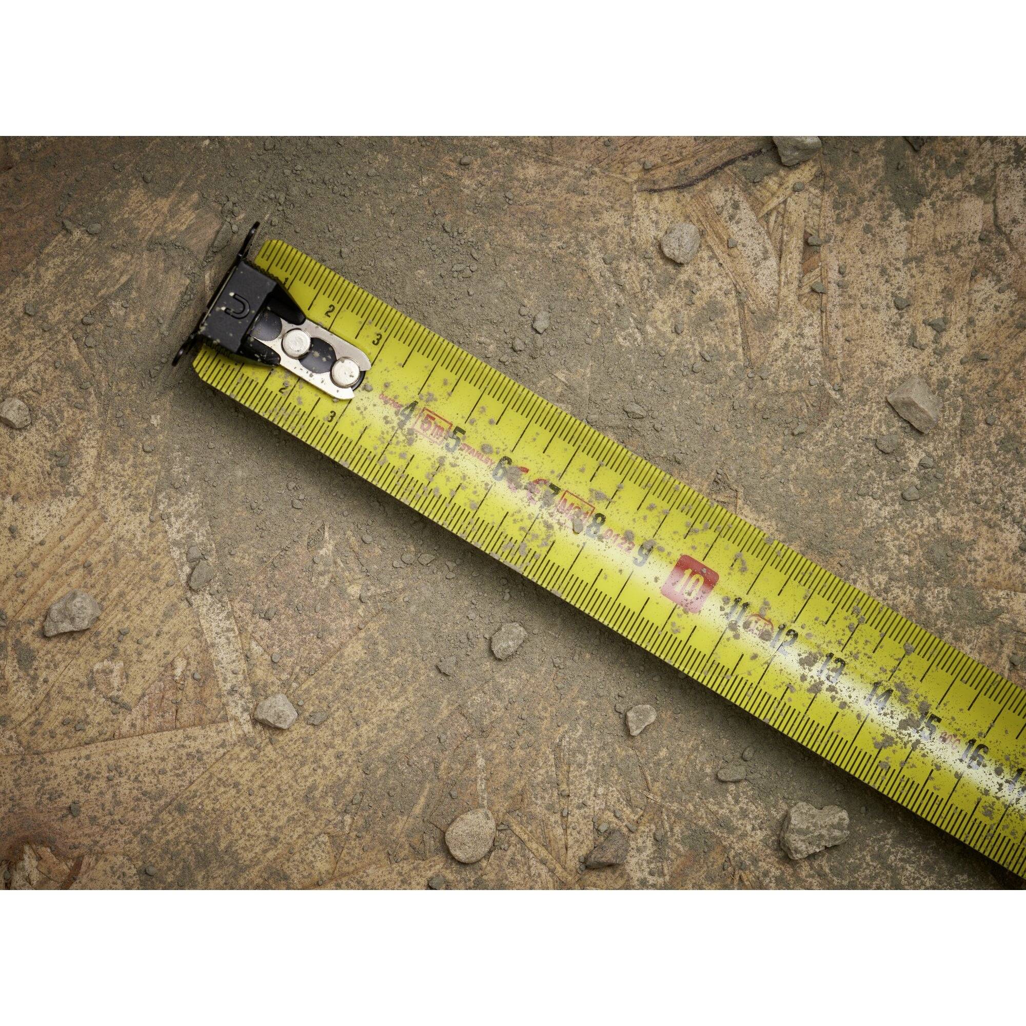 Un nastro metrico giallo è posizionato diagonalmente su un terreno sabbioso con piccoli sassi, indicando circa 17 cm.