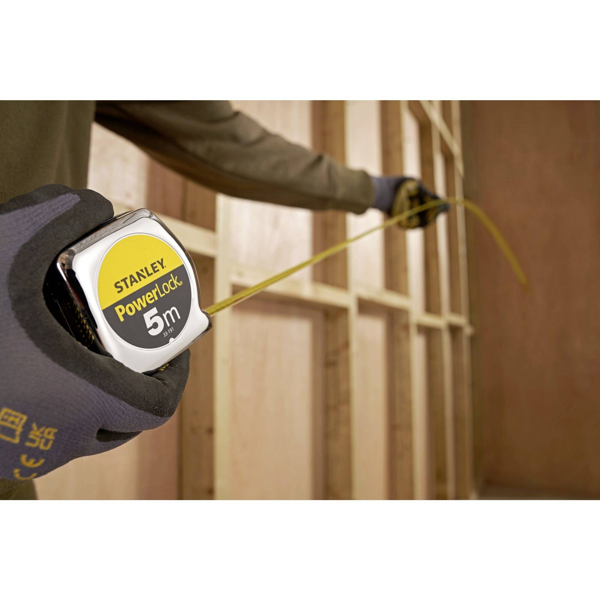 Una persona sta utilizzando un metro a nastro ('Stanley PowerLock 5m') per misurare la lunghezza di un telaio in legno.