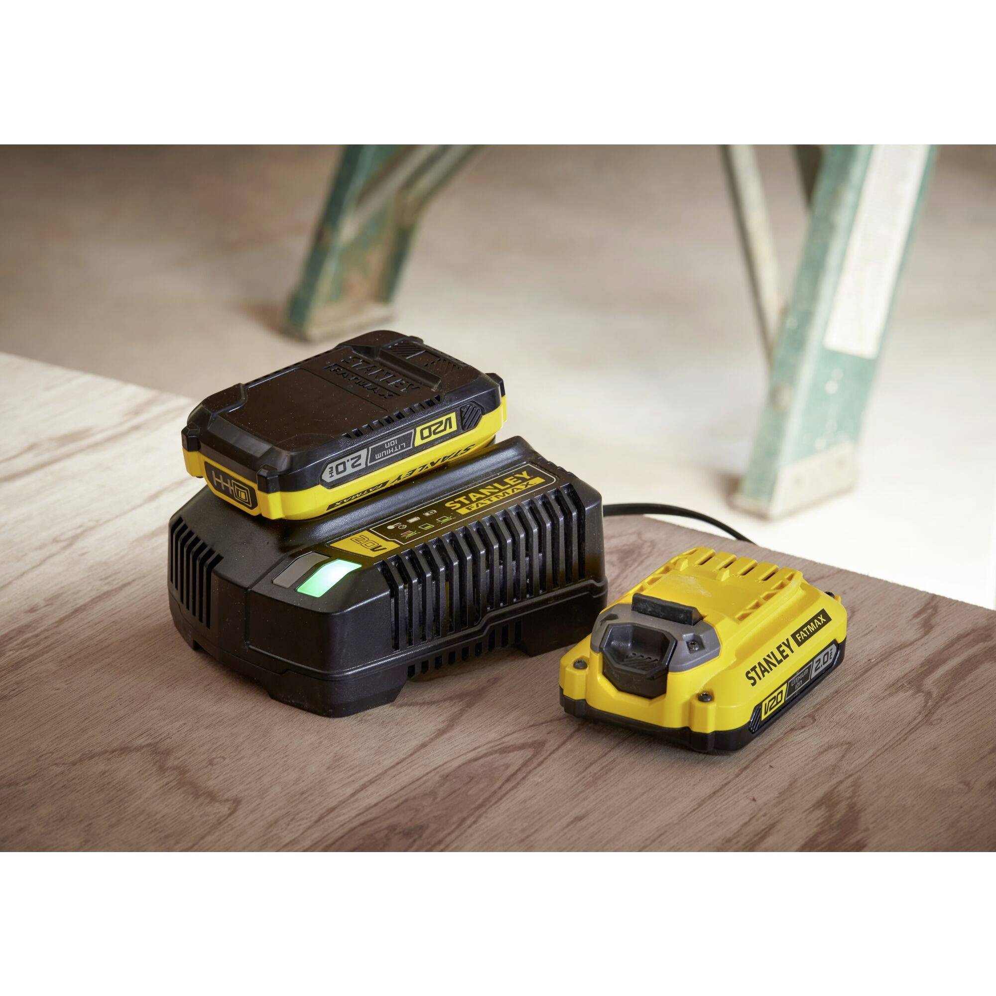 Un caricabatterie giallo sta caricando una batteria per utensili nera su un tavolo di legno. Sullo sfondo sono visibili mobili da officina.