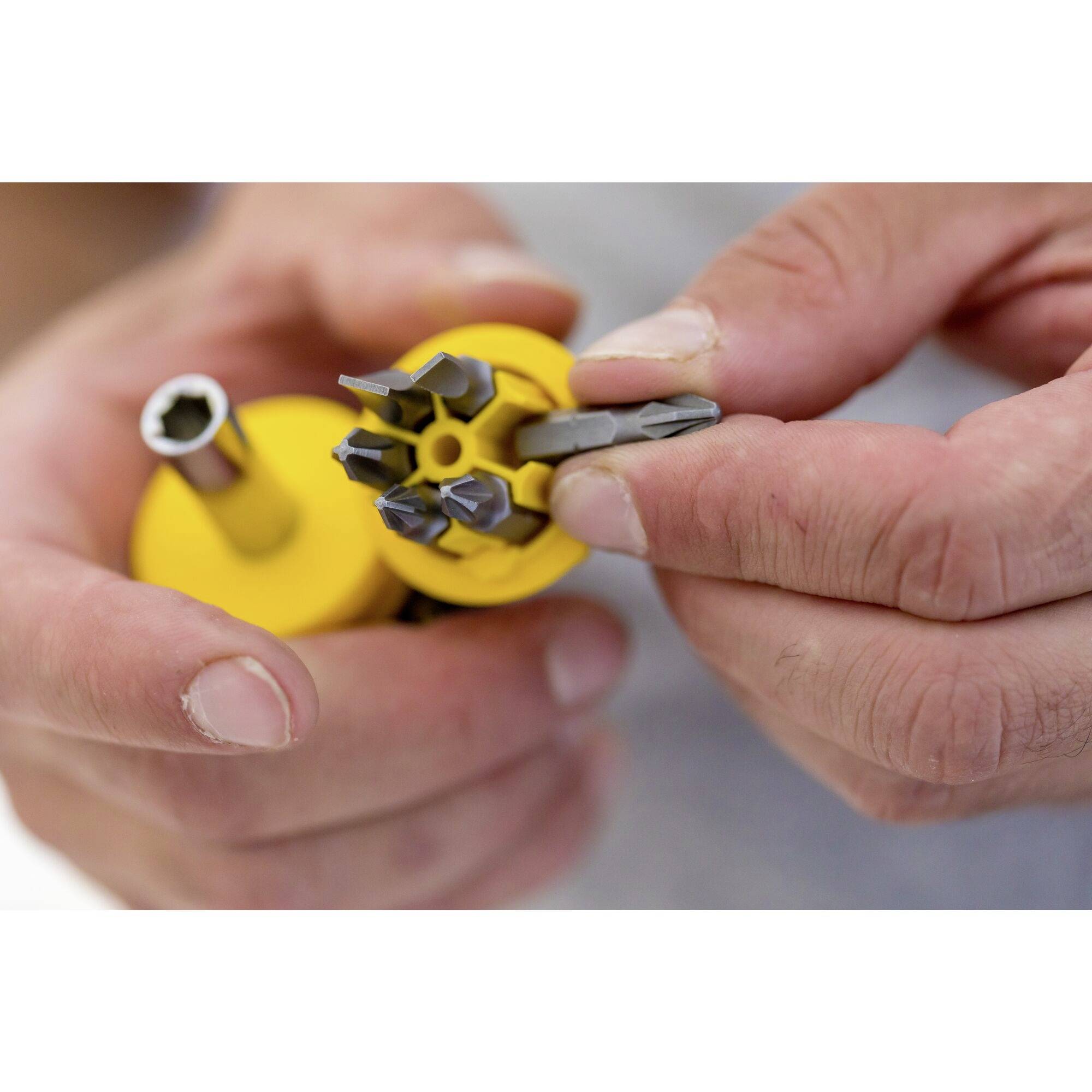 Una persona tiene in mano un supporto giallo per bit con diversi inserti per cacciavite, pronta a scegliere l'inserto più adatto.