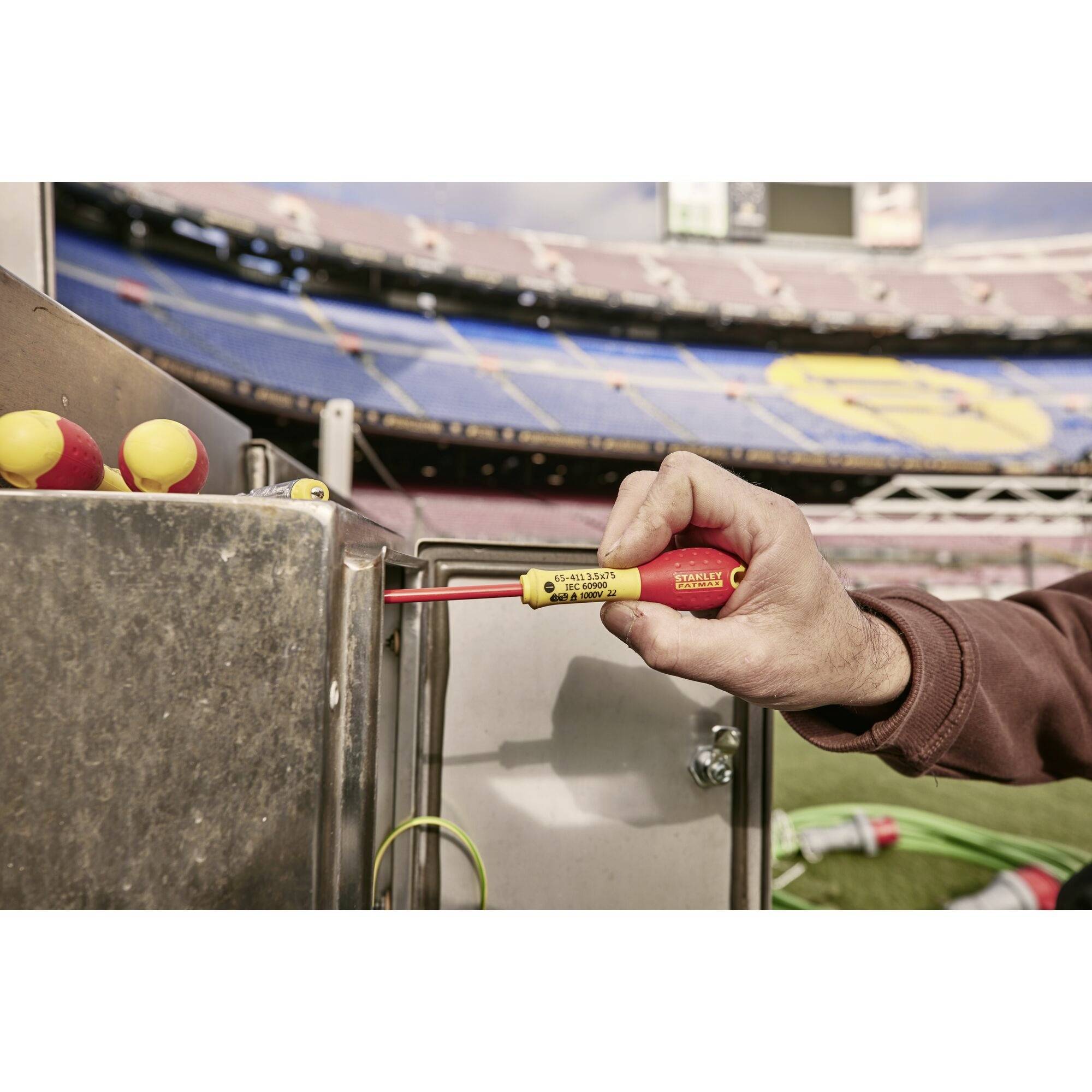 Un artigiano utilizza un cercafase su una superficie metallica all'interno dello stadio. Le tribune sono visibili sullo sfondo.