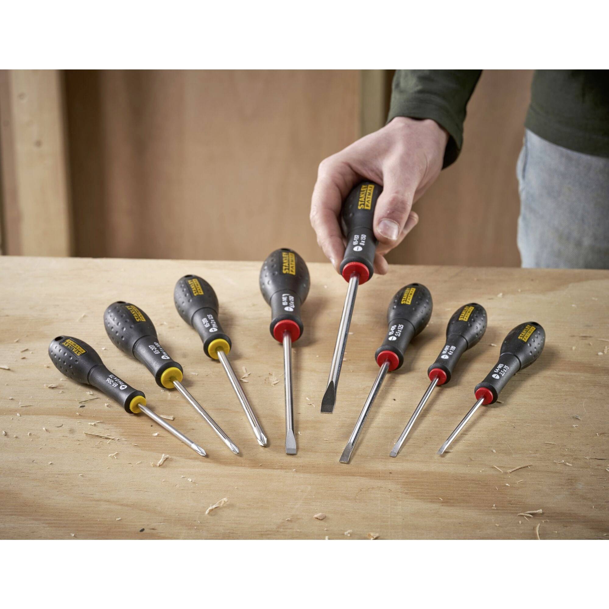 Otto cacciaviti con punte e dimensioni diverse sono posizionati su un tavolo di legno. Una mano tiene un ulteriore cacciavite.