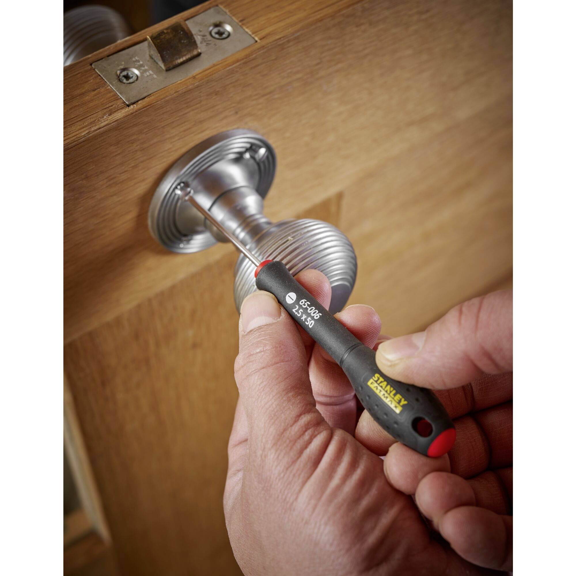 Un cacciavite viene tenuto in mano e serra una vite su di una maniglia d'argento di una porta di legno.