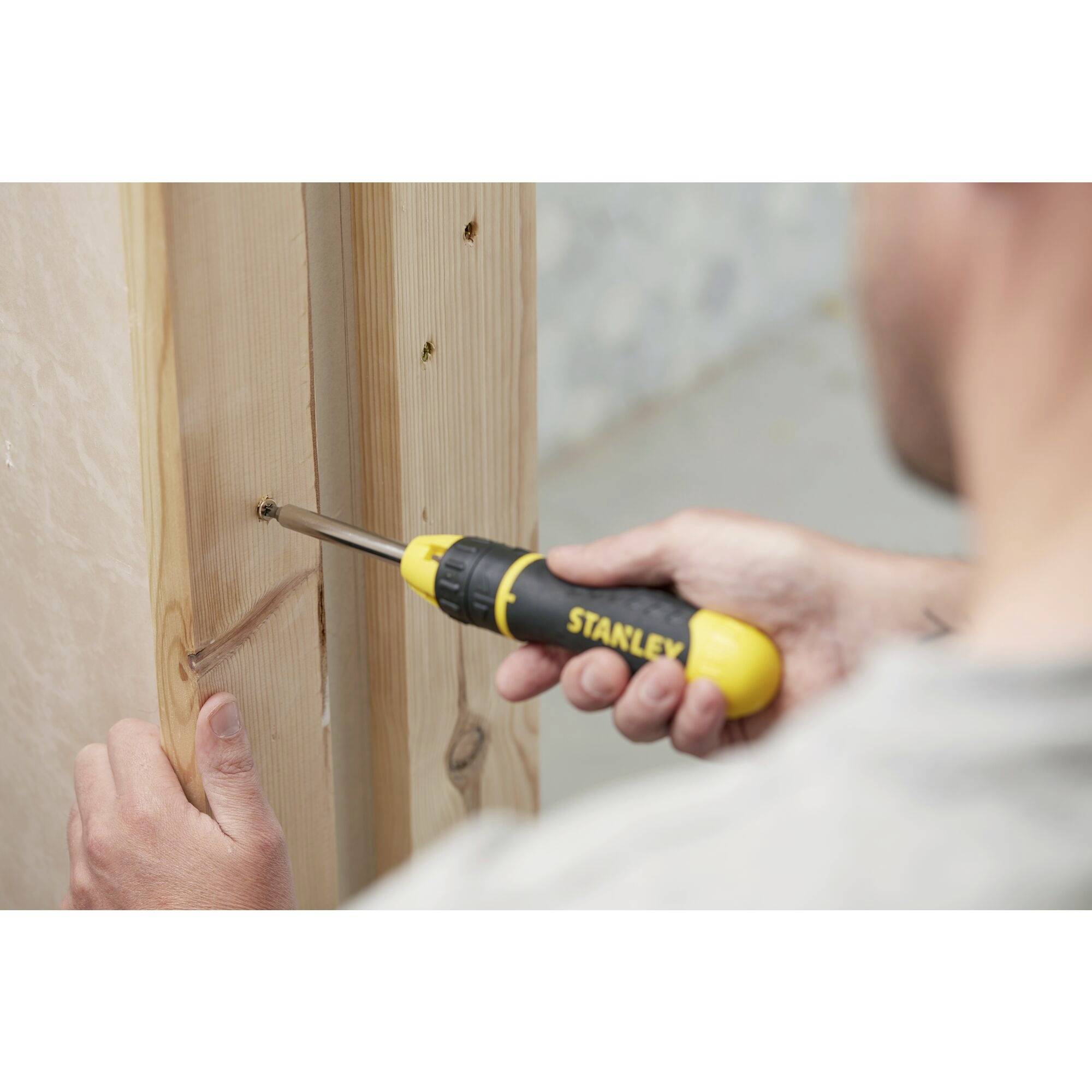 Una persona sta utilizzando un cacciavite giallo e nero per avvitare una vite in una tavola di legno.