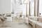 Soggiorno luminoso con divano beige, poltrona moderna, tre tavoli rotondi e cucina a vista sullo sfondo. Arredato in modo arioso e minimale.