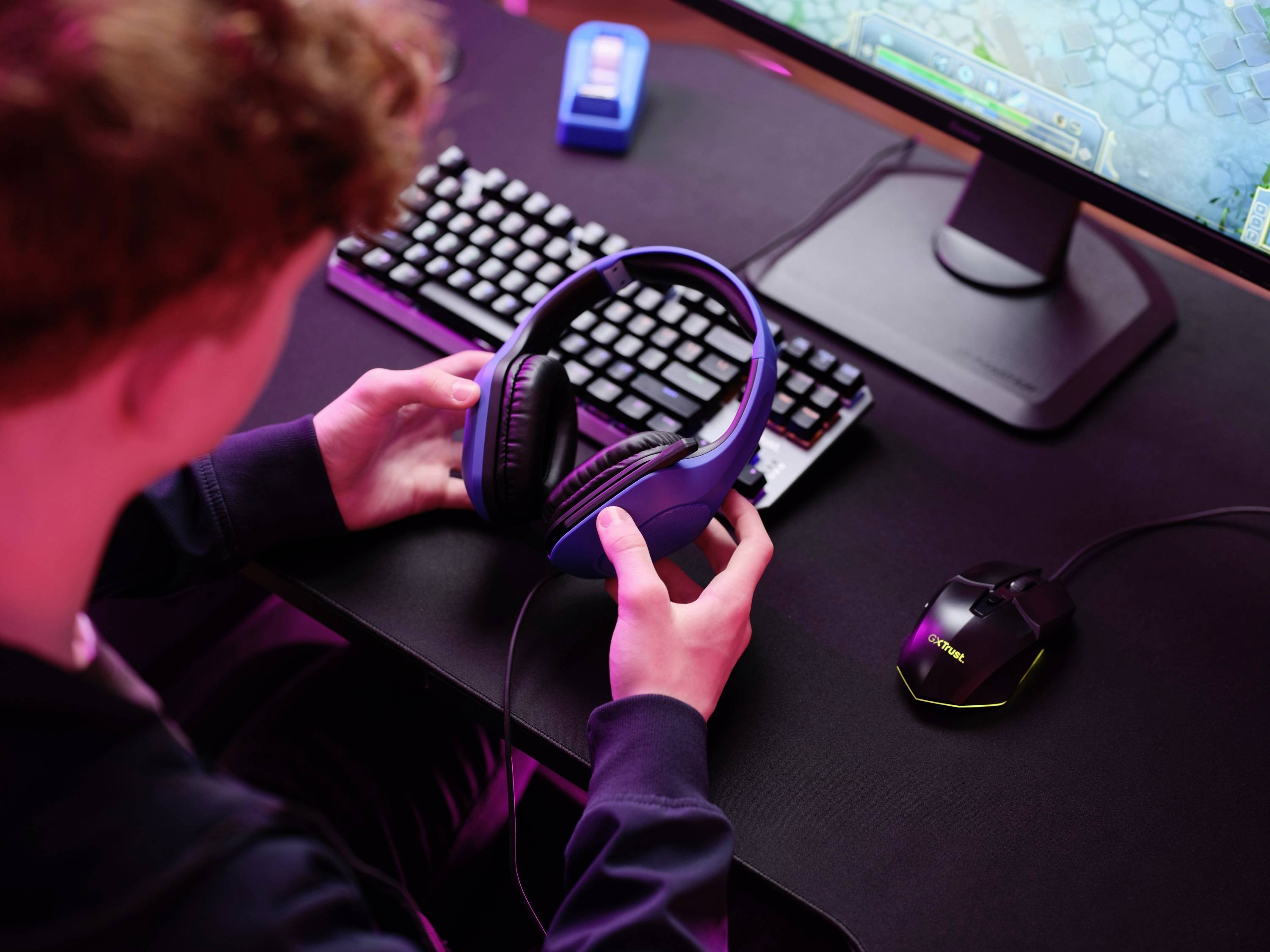 Una persona siede a una scrivania con un computer, indossa delle cuffie. Lo schermo mostra un videogioco.