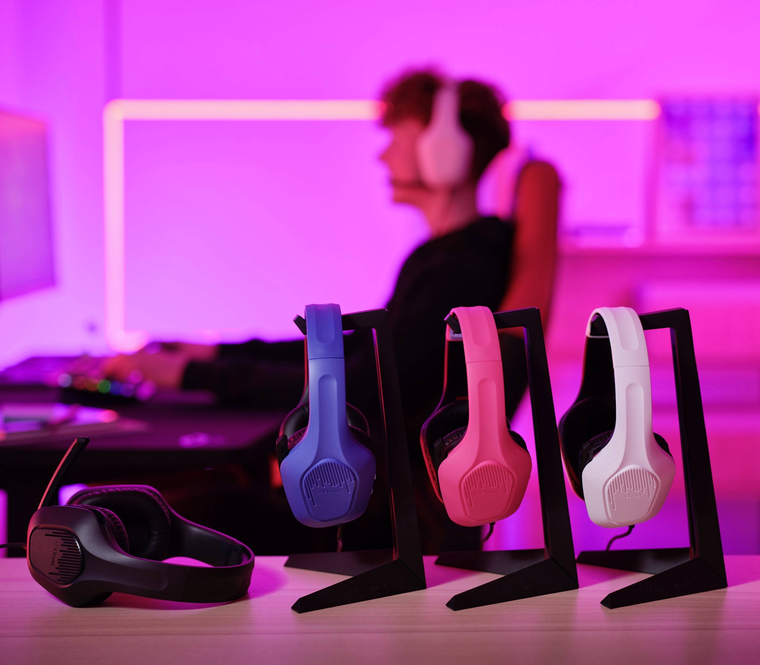 Una persona indossa un headset e siede a una scrivania davanti a uno schermo. In primo piano ci sono tre headset di colori diversi.