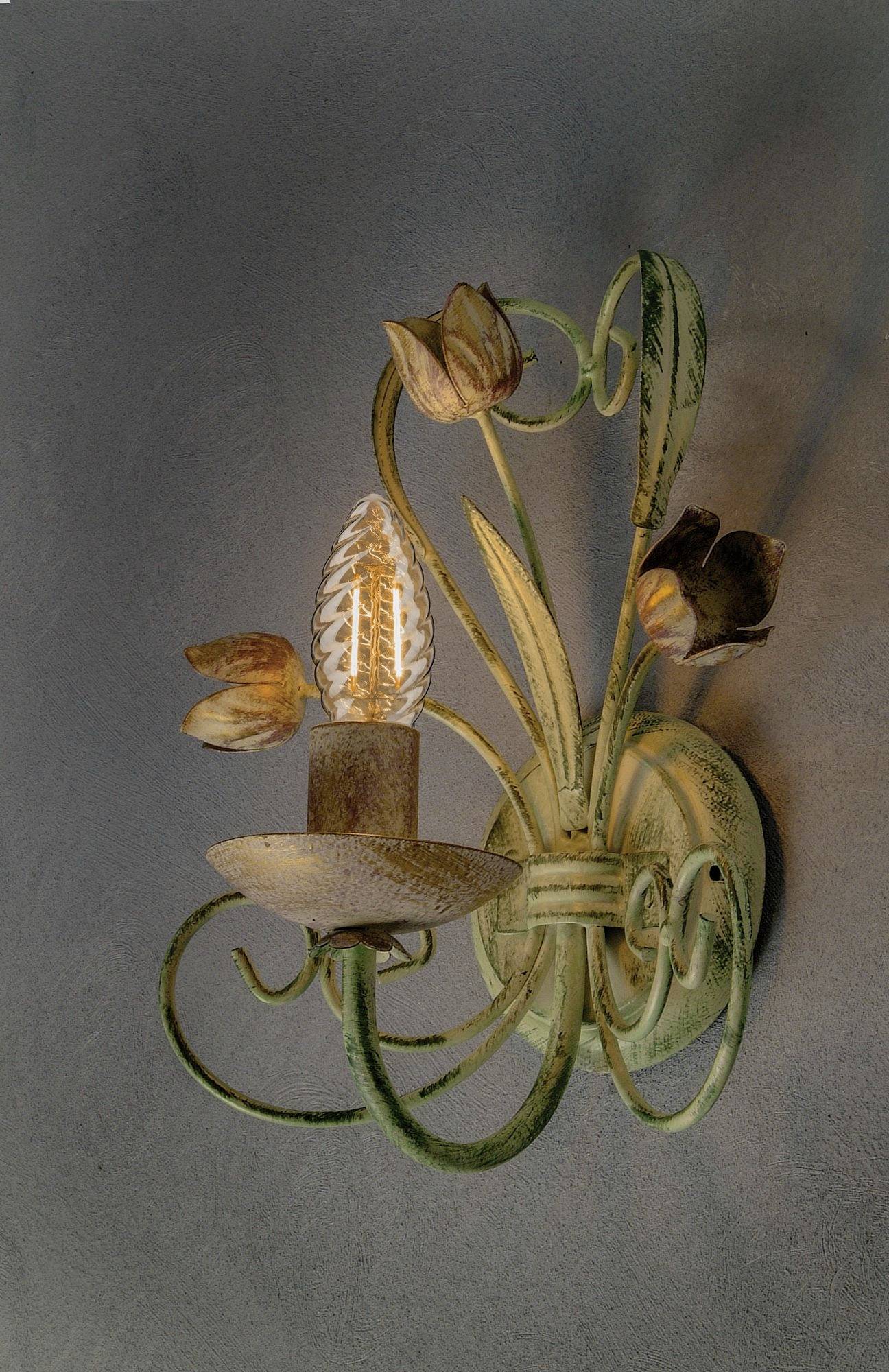 Antica applique da parete con decorazioni floreali, illumina con un calore accogliente contro un muro grigio.