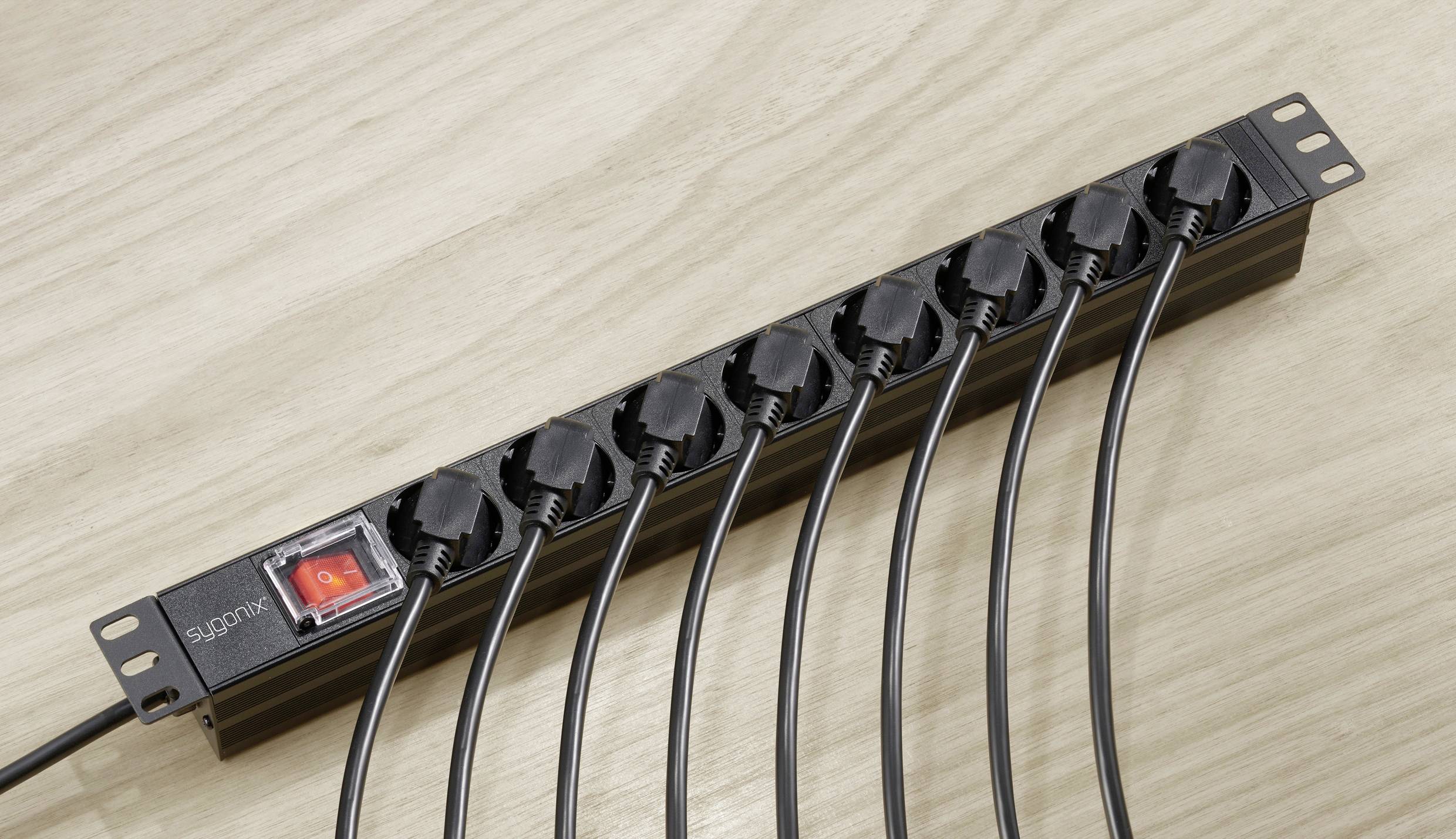 Una ciabatta elettrica nera con otto prese è posizionata su una superficie di legno. Sette spine sono inserite nelle prese.