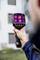 Una persona tiene una termocamera, mostrando un edificio con differenze di temperatura visibili sul display.