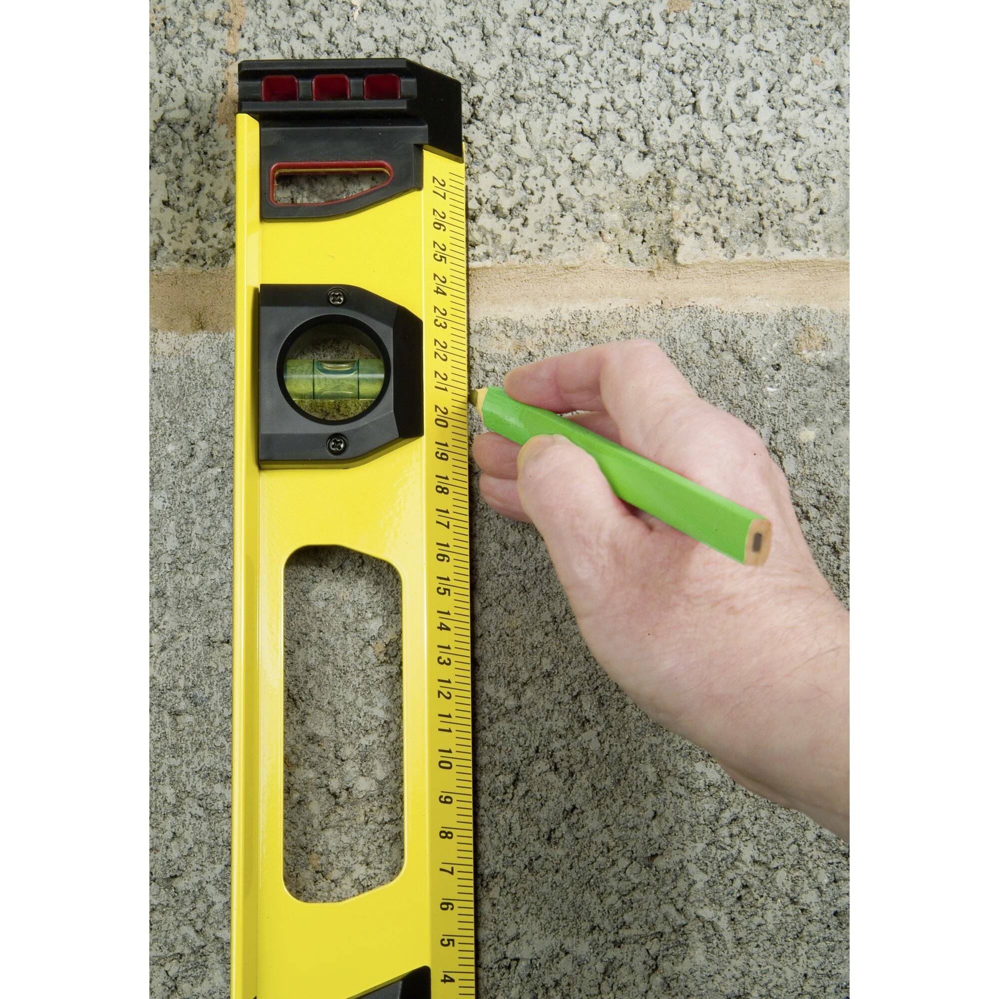 Una mano contrassegna la posizione su un muro con un pennarello verde, mentre un livello giallo viene utilizzato per l'allineamento.