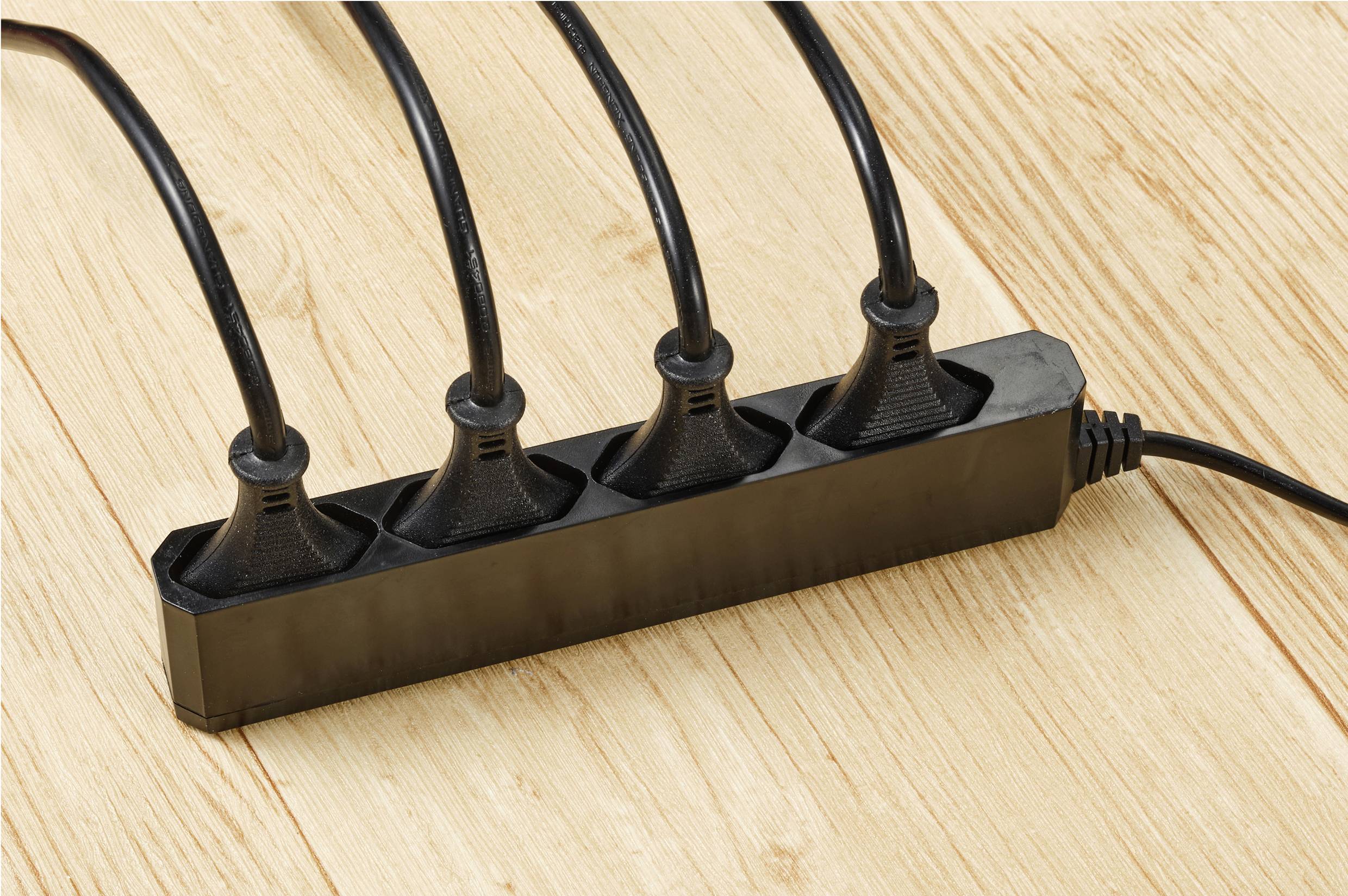 Una presa multipla nera con cinque cavi neri inseriti è posizionata su un pavimento di legno.