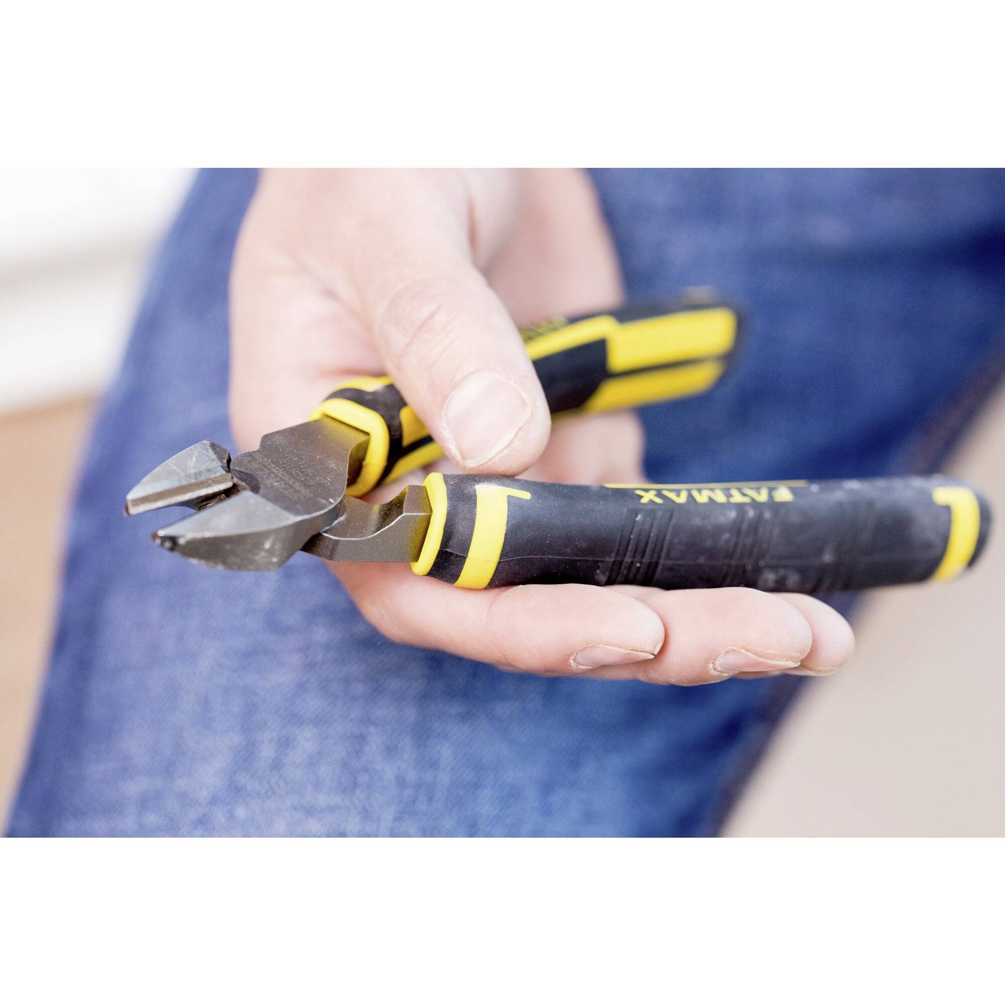 Una mano tiene un tronchese giallo-nero con la scritta 'ATAK'. Lo sfondo è sfocato, la persona indossa jeans.