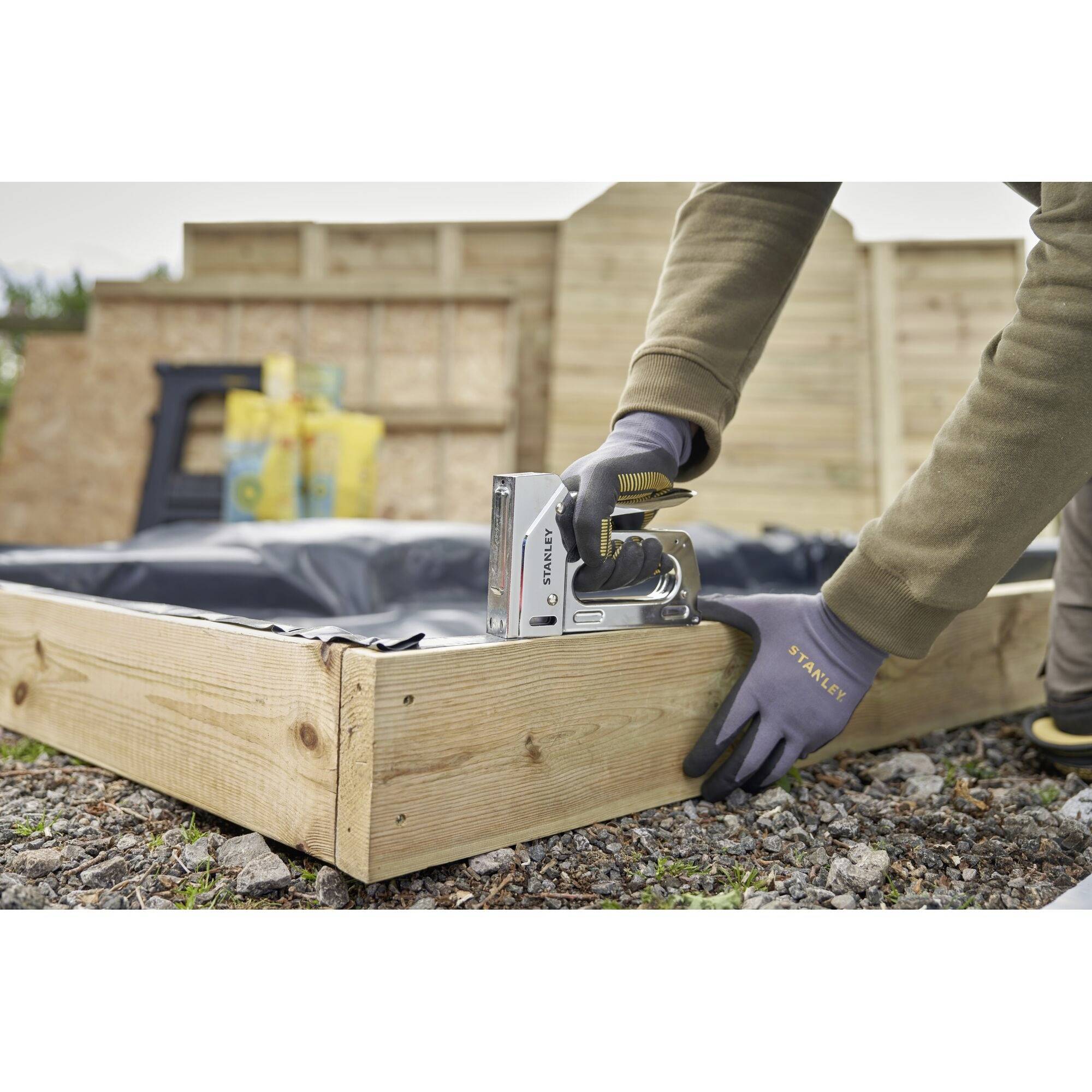 Una persona costruisce una scatola di legno rettangolare all'aperto. Utilizza un utensile elettrico per fissare le tavole di legno.