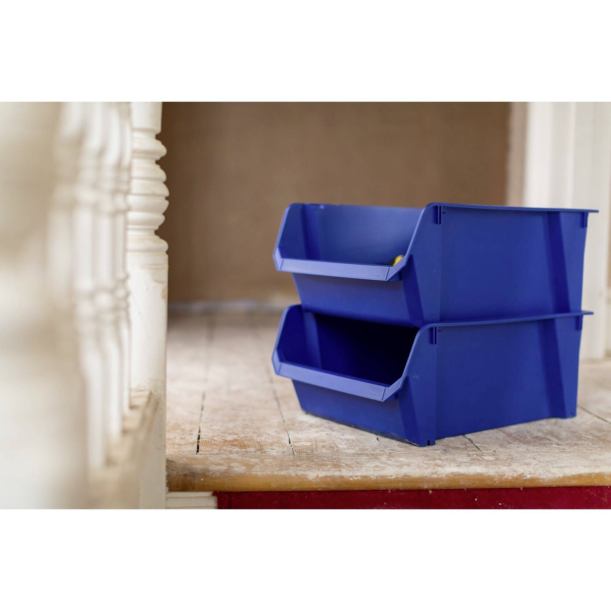 Due scatole di plastica blu impilate l'una sull'altra sono poste su un pavimento di legno accanto a una balaustra bianca.