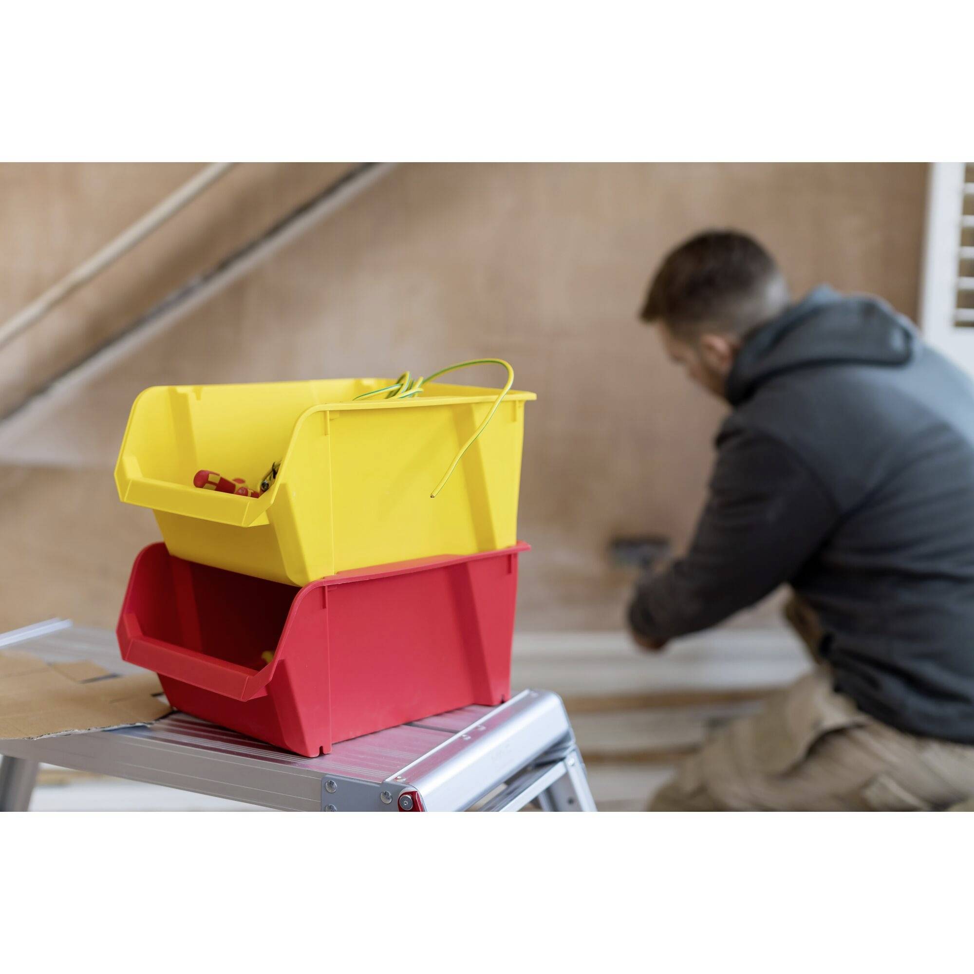 Due scatole di plastica colorate sono poggiate su una scala, mentre una persona sullo sfondo sta dipingendo un muro.
