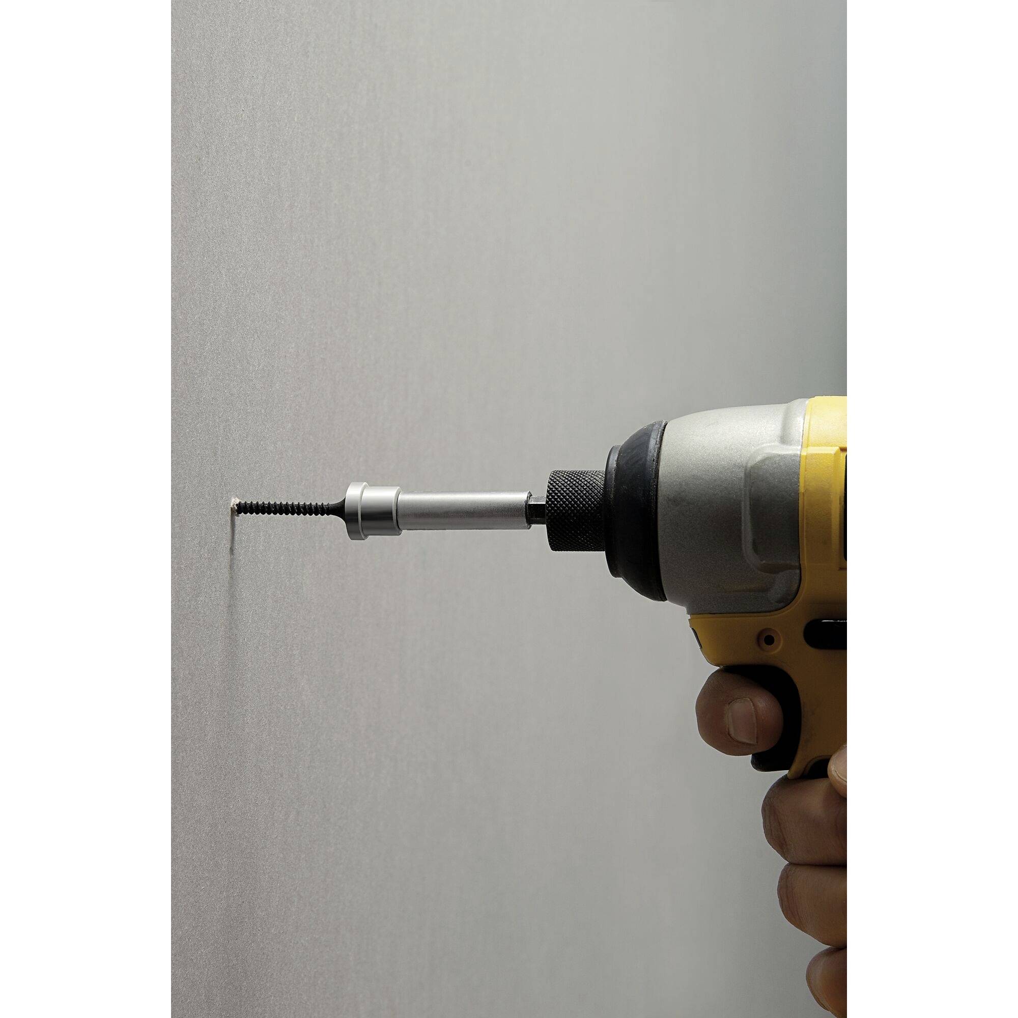 Una mano tiene un trapano avvitatore giallo che sta avvitando una vite in un muro grigio.