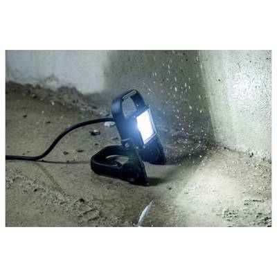Lampada da lavoro portatile su un pavimento in cemento, che illumina un muro con polvere o gocce d'acqua nell'aria.