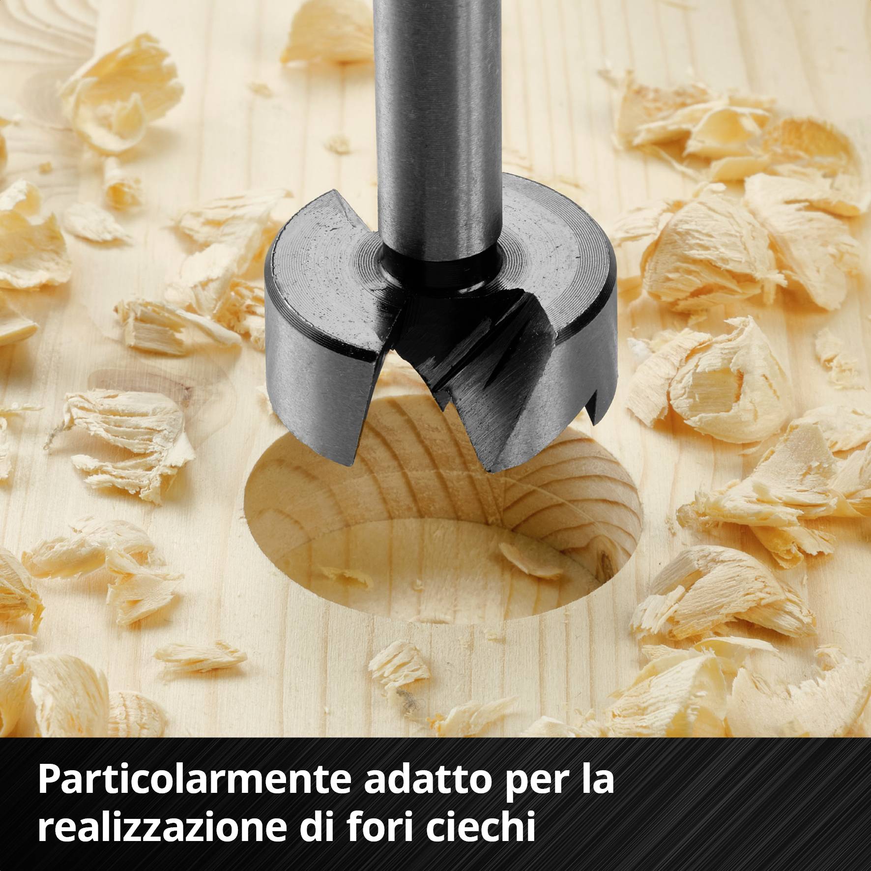 Un trapano per legno metallico in azione, trapana un foro circolare nel legno, circondato da trucioli. Testo: 'Particolarmente adatto per la realizzazione di fori ciechi'.