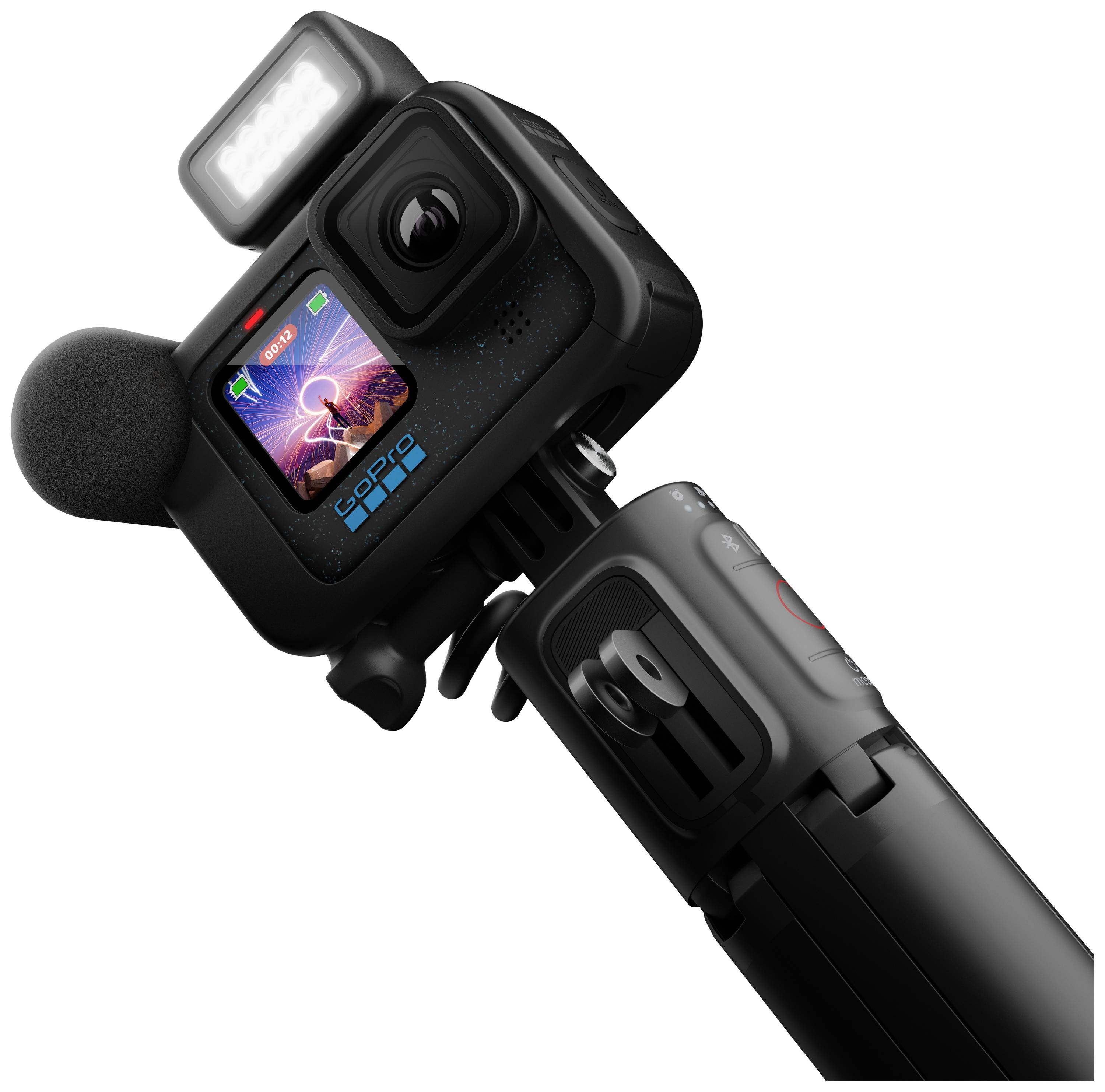 Una action camera con microfono e luce montati mostra un'immagine colorata sul suo display. La fotocamera è fissata su un treppiede.