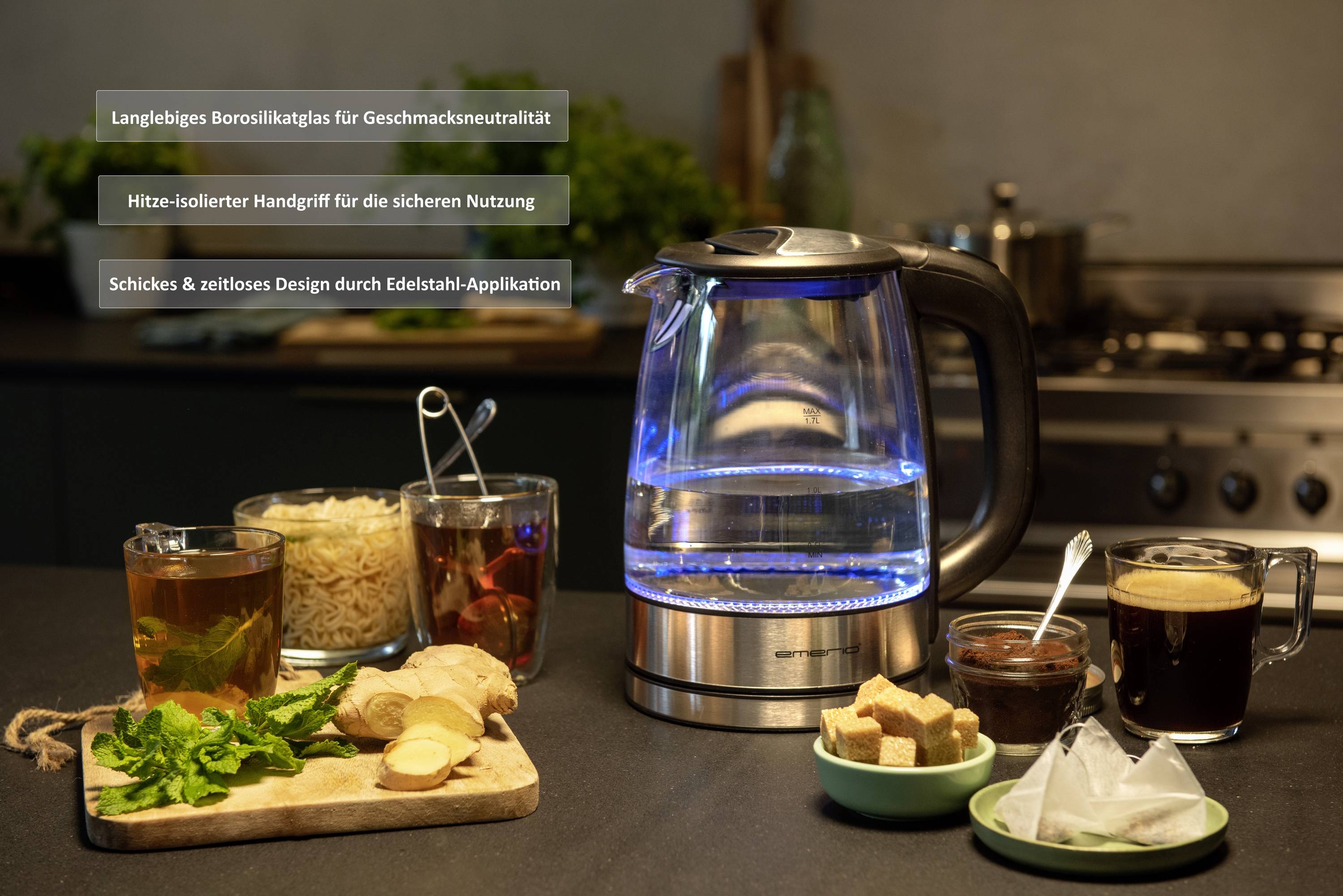 Un bollitore in vetro con illuminazione LED blu è posizionato su un piano di lavoro della cucina. Accanto sono sistemati ingredienti per tè e caffè.