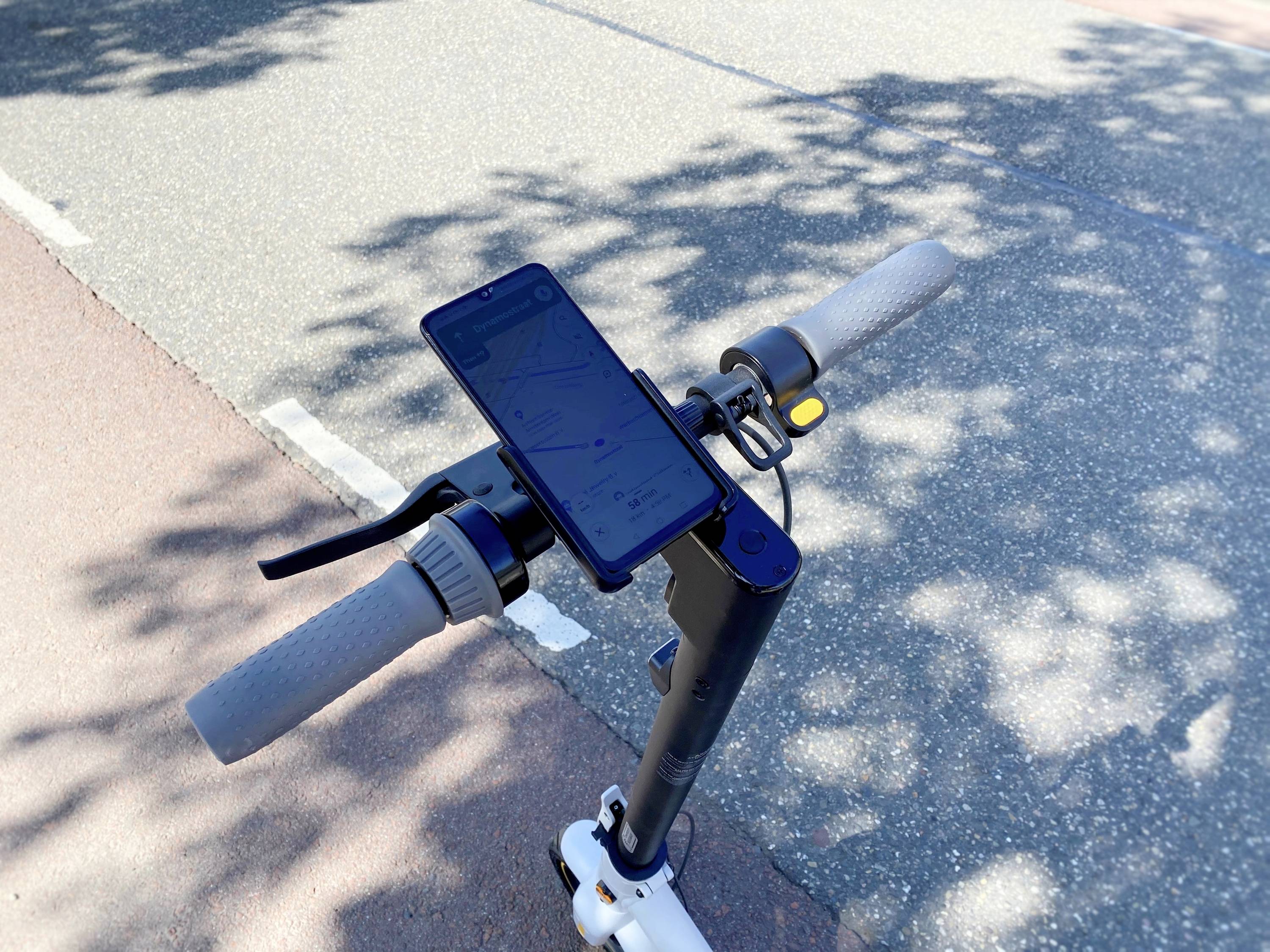 Un monopattino elettrico con un supporto per smartphone sul manubrio che mostra un'app di navigazione. Il monopattino è fermo su un percorso asfaltato.