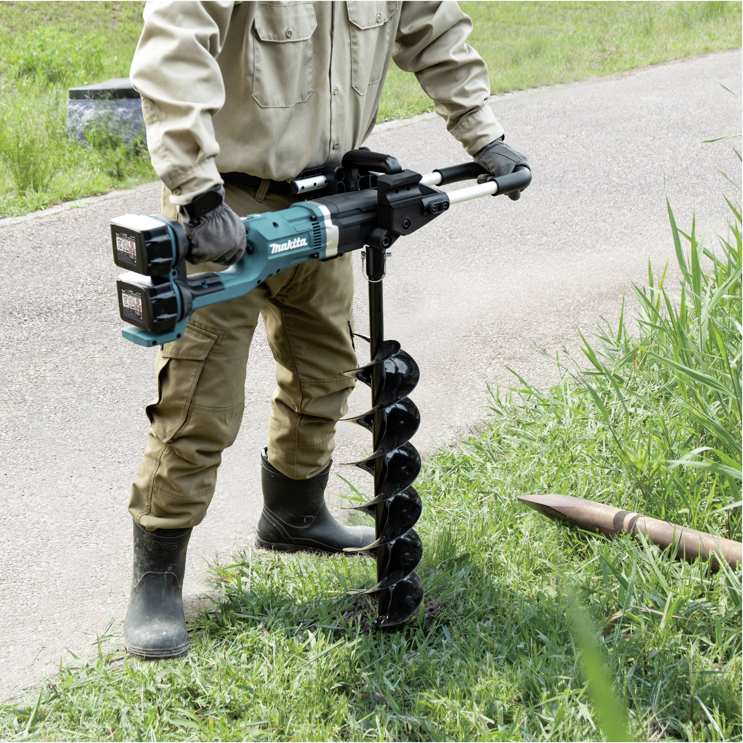 Una persona trapana nel terreno accanto a un ciuffo d'erba usando una trivella elettrica. Cielo terso, con l'attenzione concentrata sull'attrezzo.