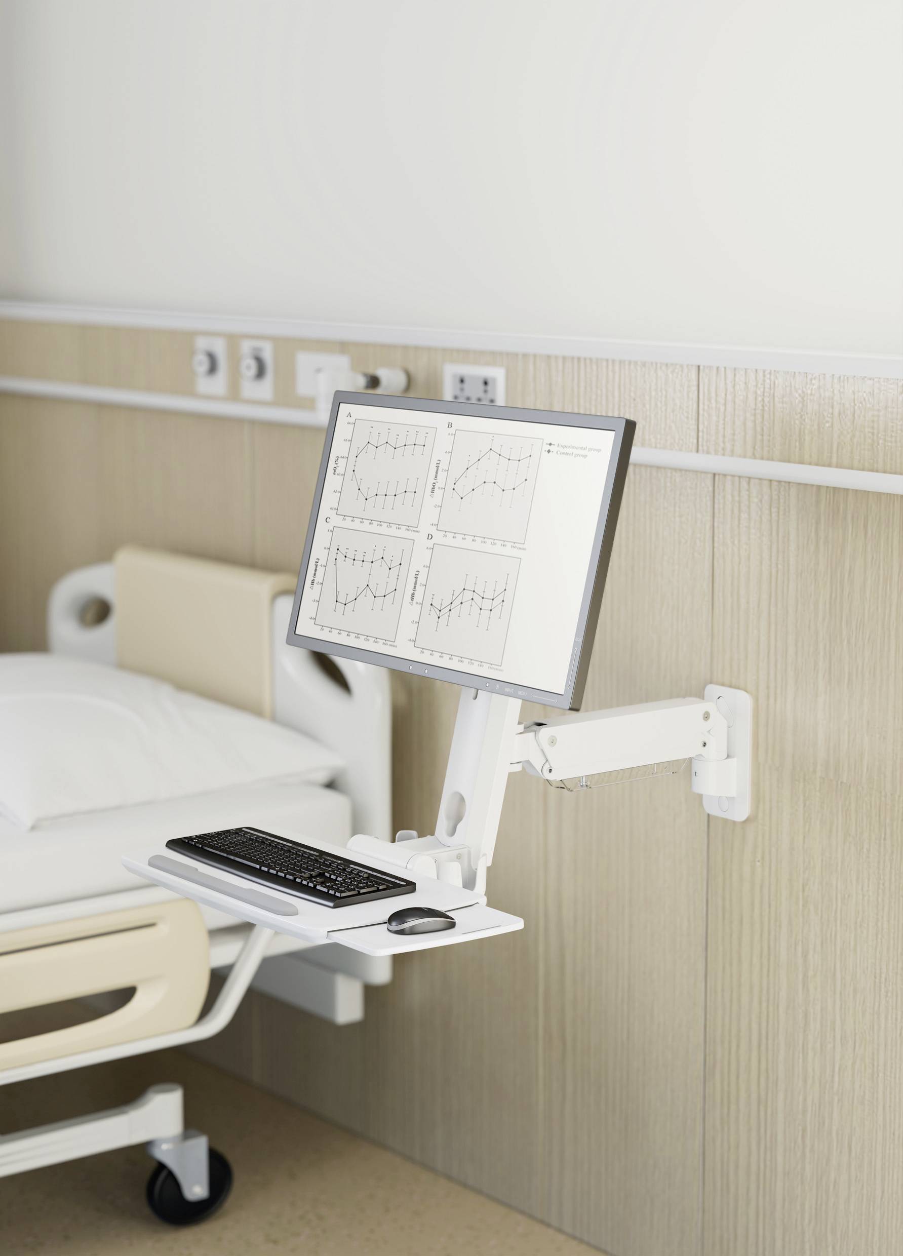 In ospedale, un monitor accanto a un letto di degenza mostra diagrammi medici. Accanto a esso, è posizionata una tastiera su un tavolo mobile.