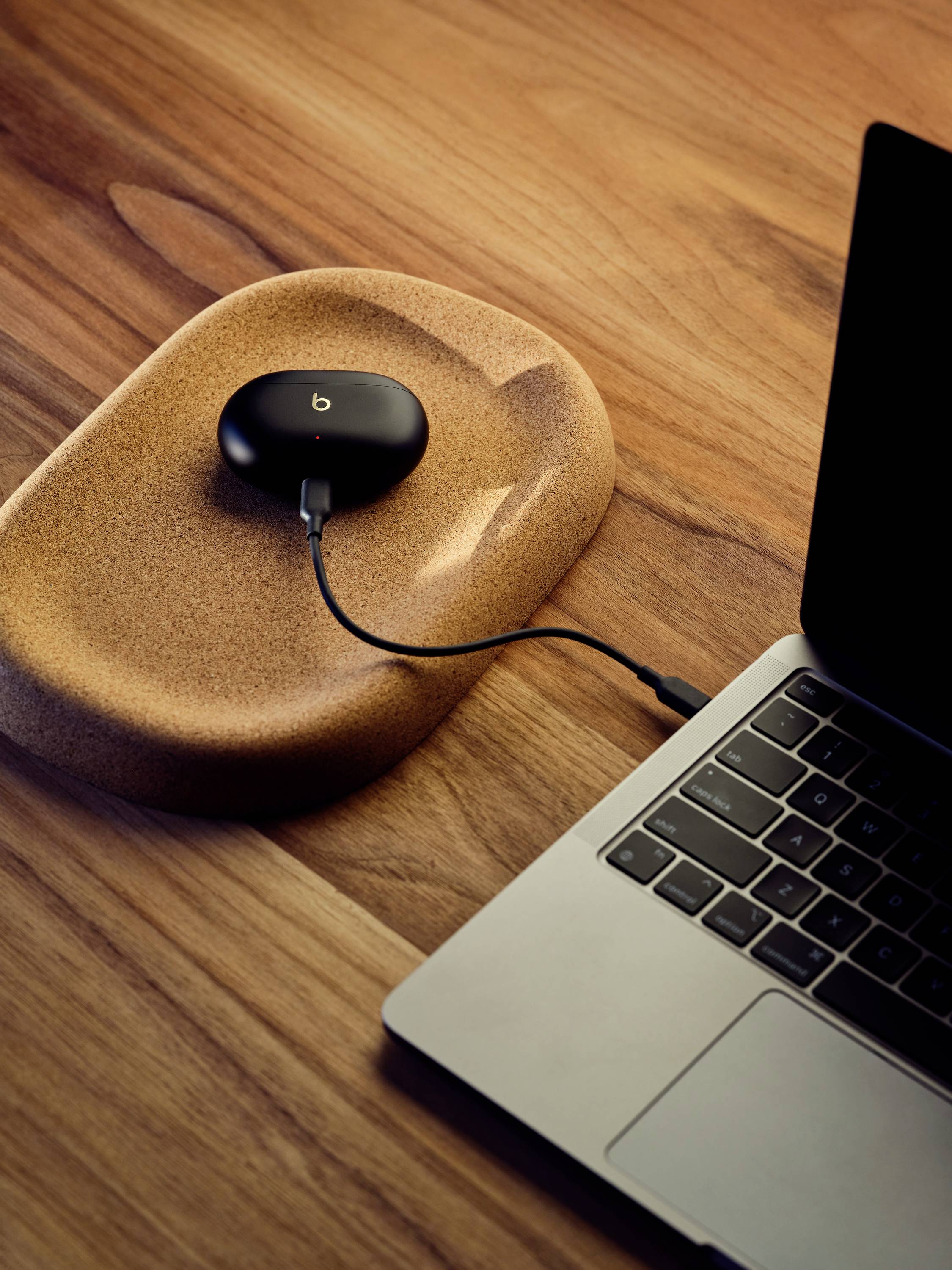 Un laptop è poggiato su un tavolo di legno, accanto a un piccolo dispositivo nero e rotondo che sta caricando.