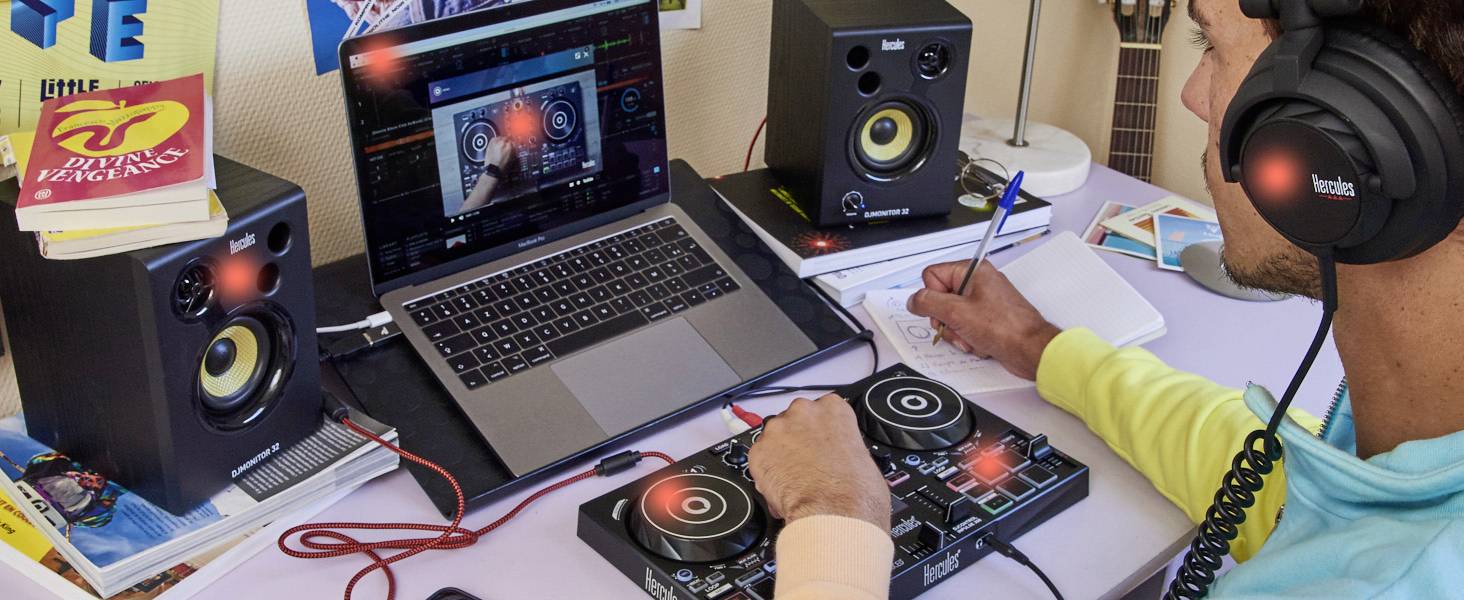 Una persona indossa delle cuffie e utilizza un controller per DJ davanti a un laptop. Altoparlanti e un quaderno sono sul tavolo.