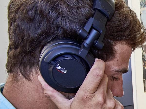 Una persona indossa cuffie nere e ascolta musica con concentrazione. Le cuffie hanno un logo 'Hercules' sul padiglione auricolare.