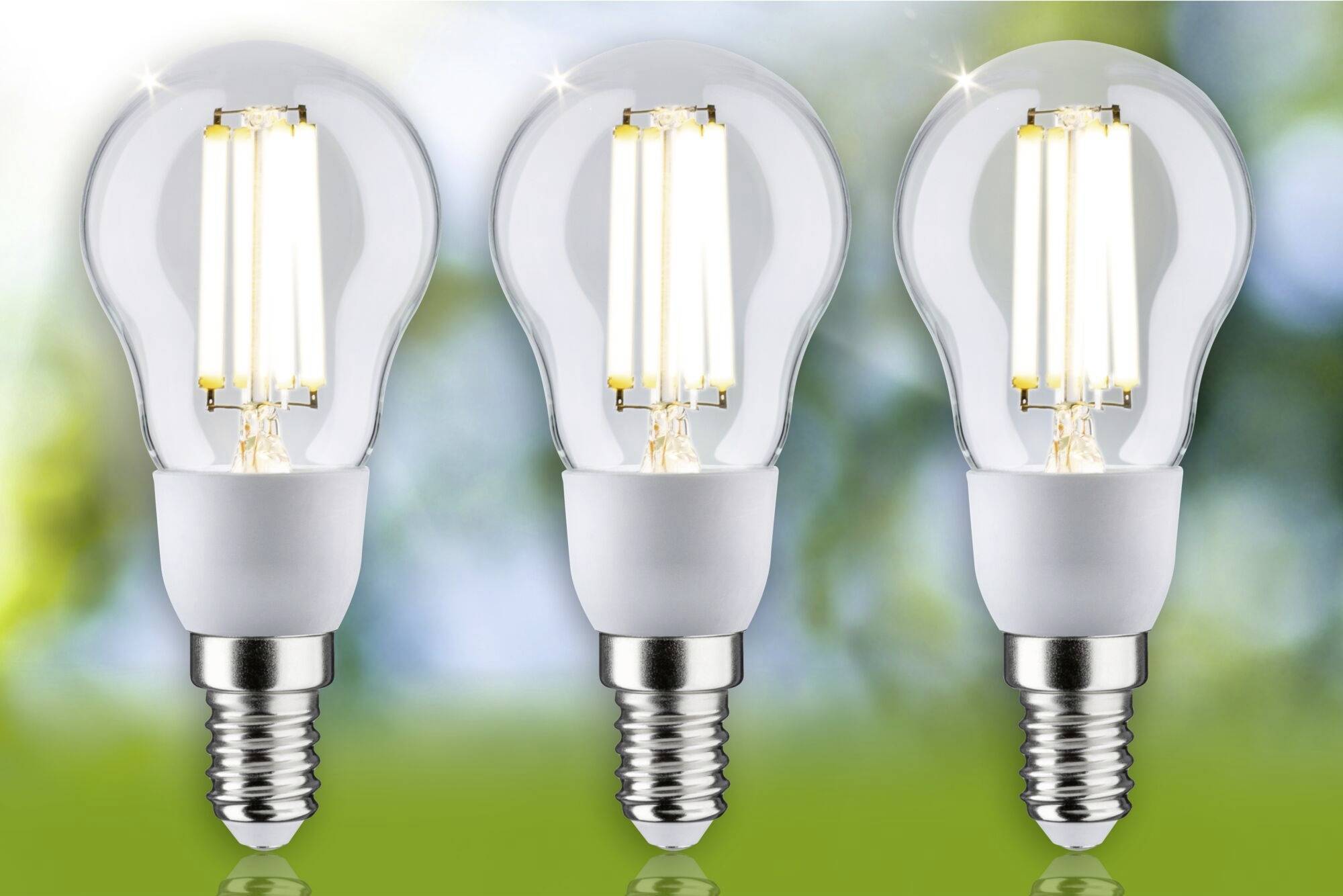 Tre lampadine LED accese davanti a uno sfondo sfocato verde e blu, simbolo di efficienza energetica.