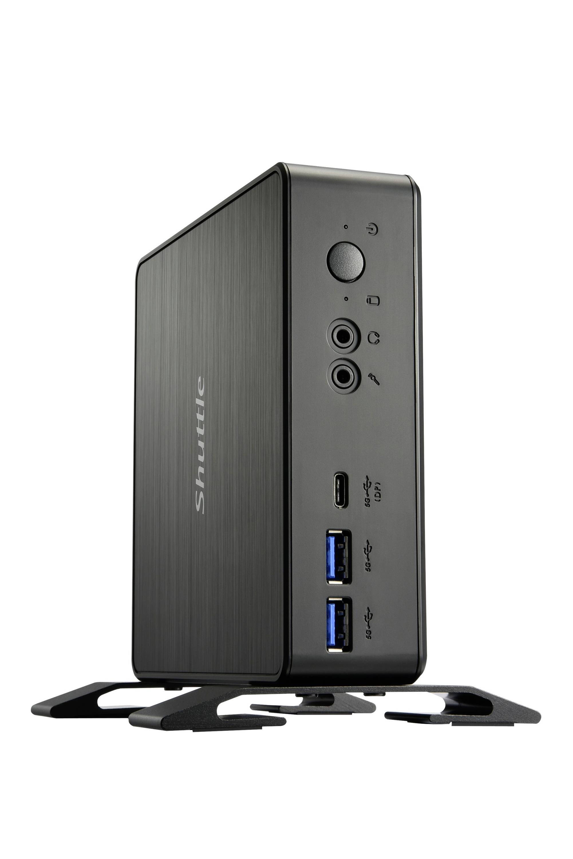 Un mini PC Shuttle nero è in posizione verticale sul suo supporto. Il lato anteriore mostra porte USB, jack audio e un pulsante di accensione.