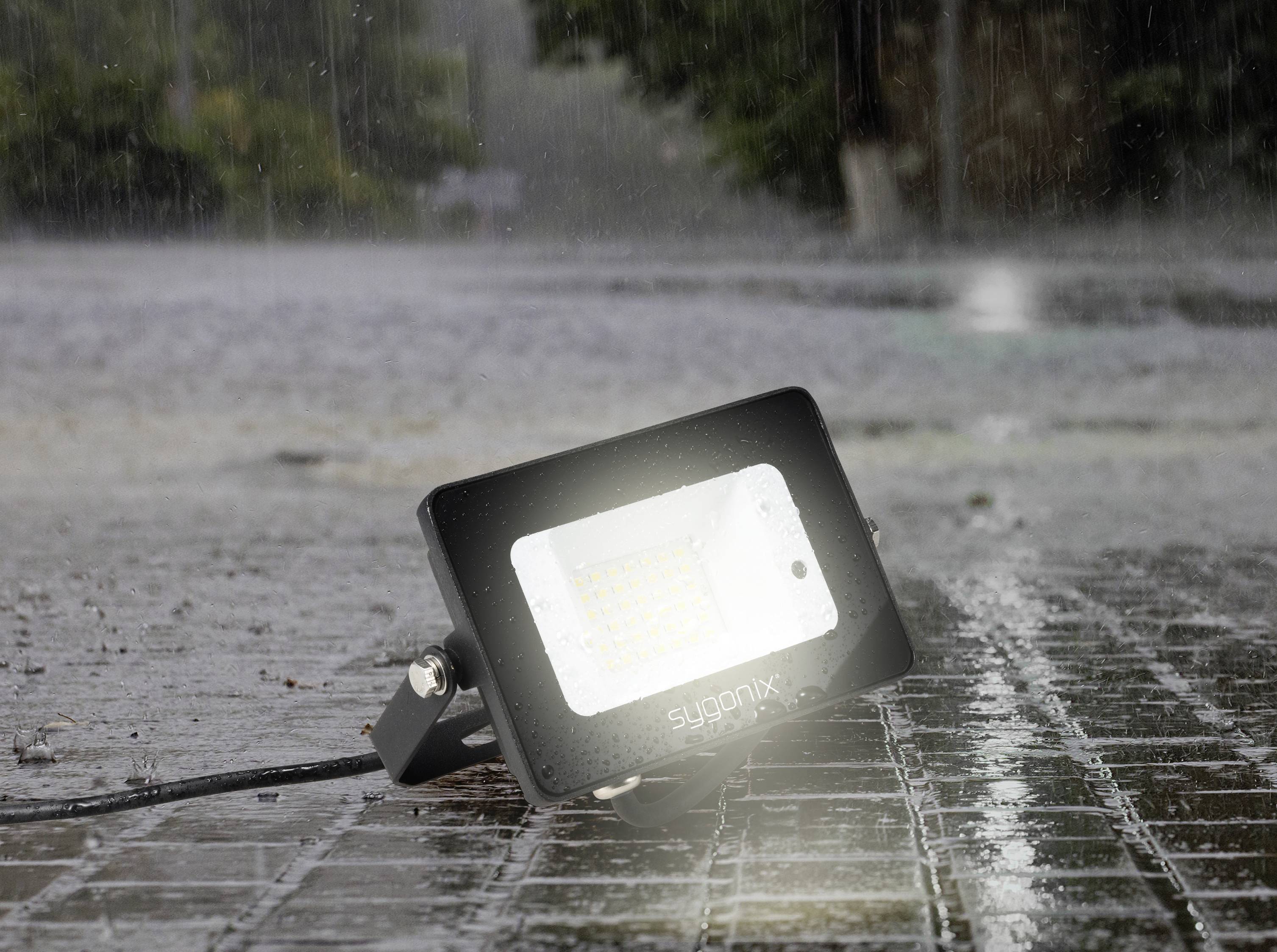 Un proiettore LED luminoso giace sulla strada bagnata acciottolata sotto la pioggia, con l'acqua che schizza tutto intorno.
