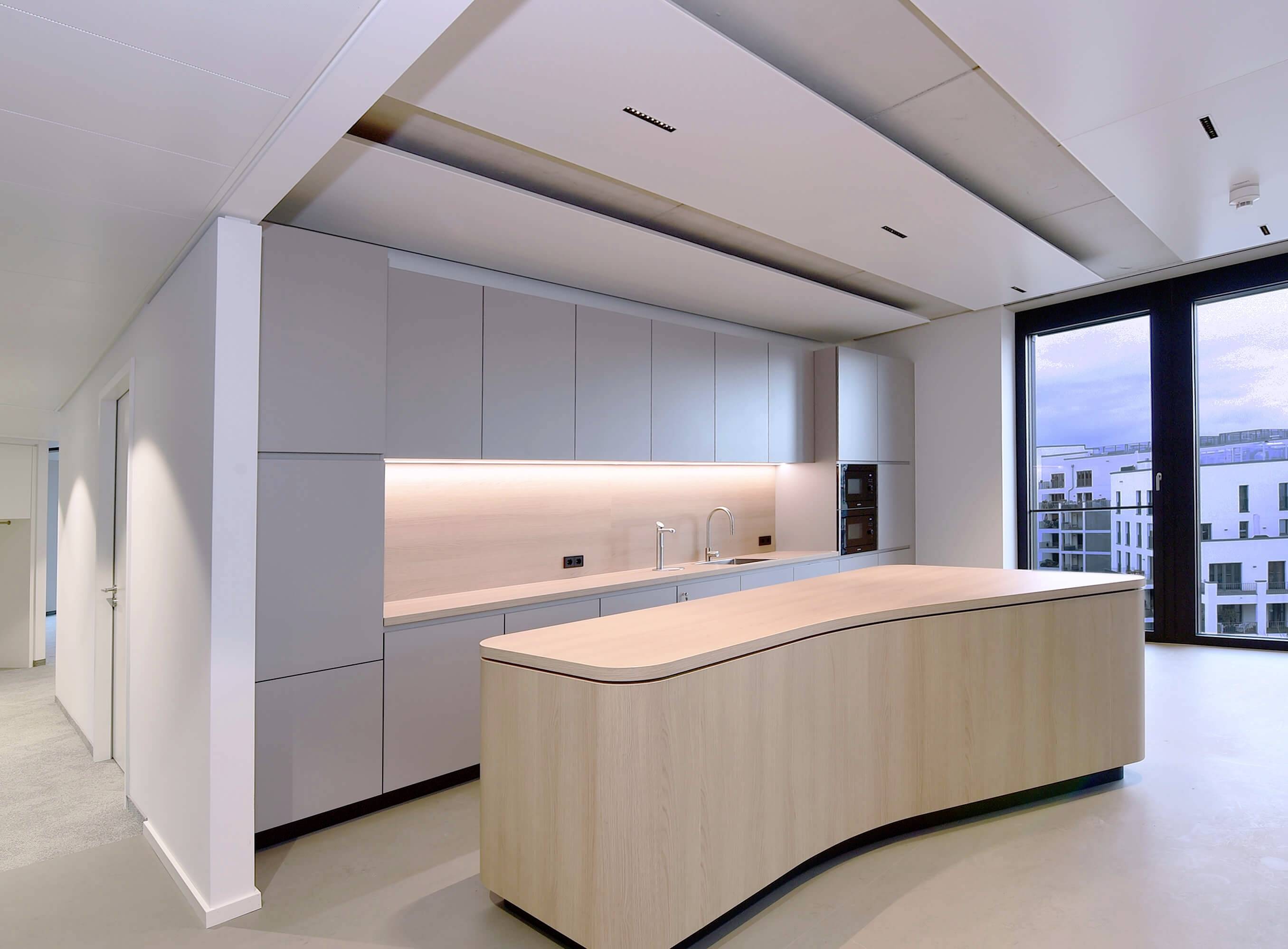 Cucina moderna con un'isola curva in legno, armadi bianchi e grandi finestre. Design luminoso e minimalista.