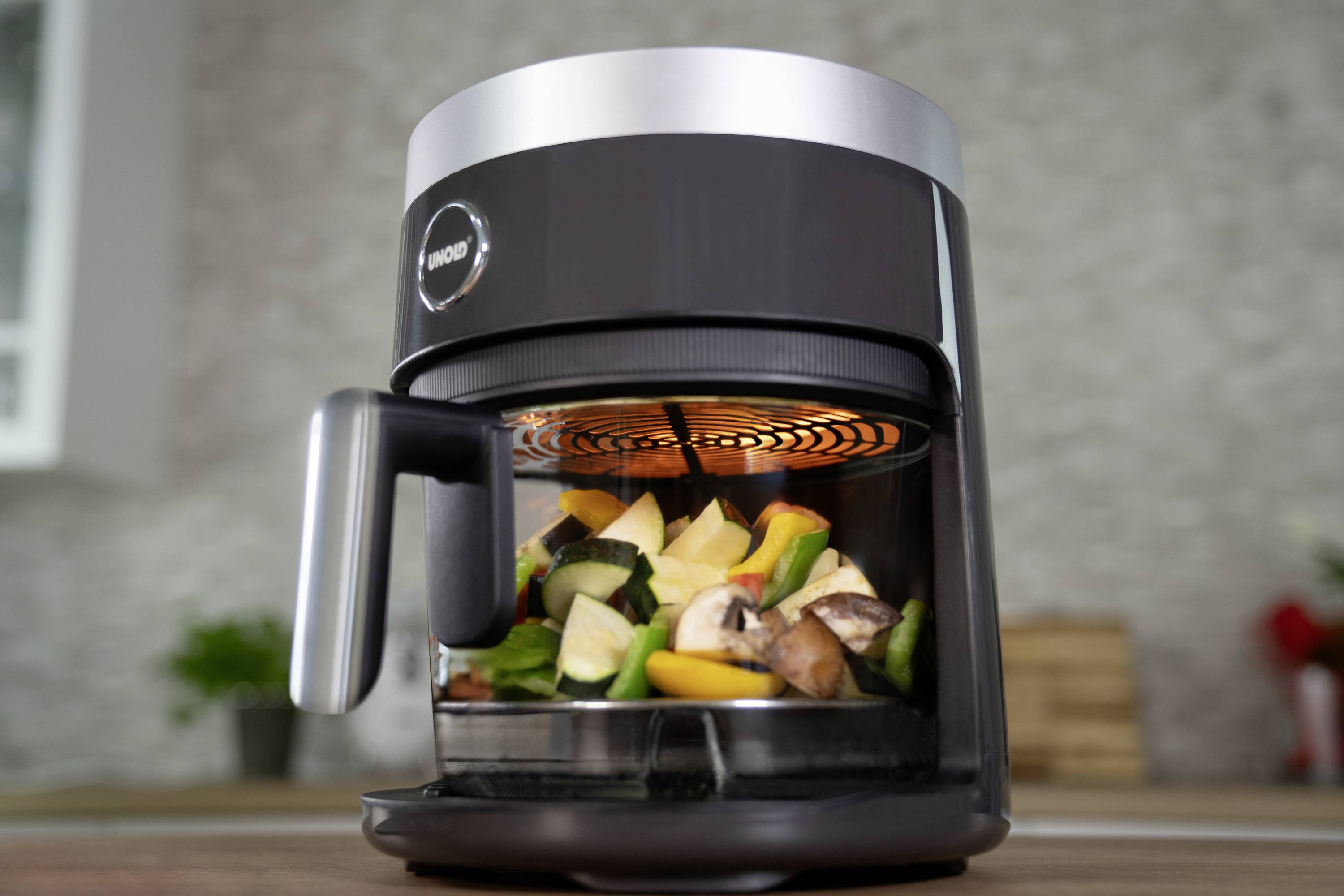 Un moderno airfryer con il coperchio aperto, riempito con verdure colorate come peperone, zucchina e funghi.