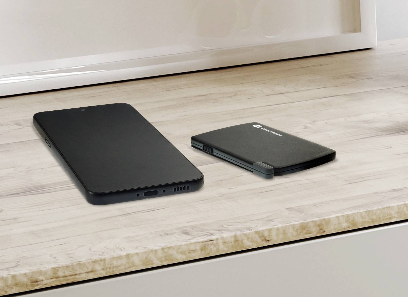 Smartphone e dispositivo mobile pieghevole su un tavolo color legno, entrambi chiusi.