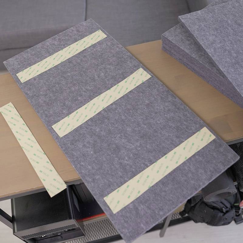 Un pezzo rettangolare di feltro grigio è posizionato su un tavolo. Su di esso sono presenti due strisce di nastro biadesivo. Accanto ci sono altri pezzi di feltro.