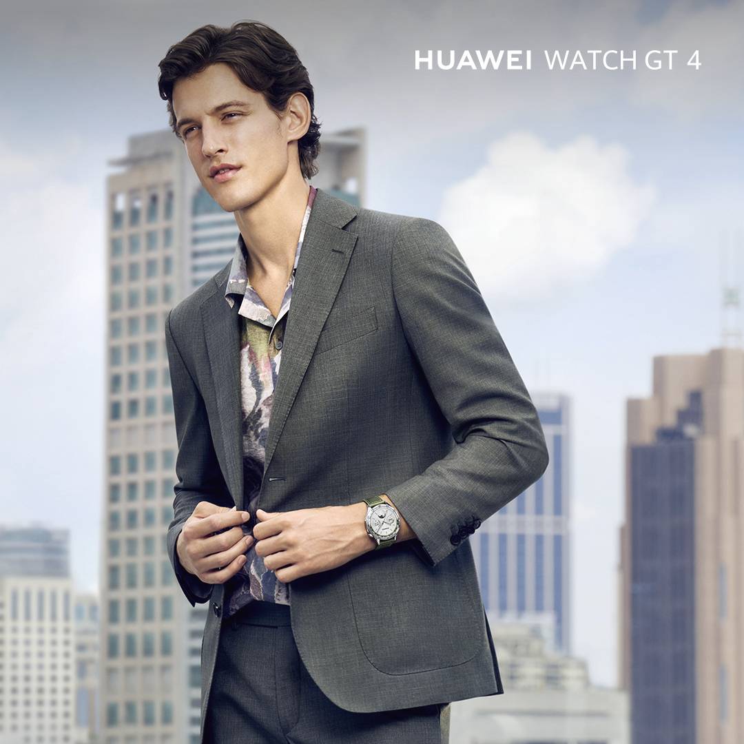 Un uomo in abito è in piedi davanti a una skyline urbana e indossa un Huawei Watch GT 4.