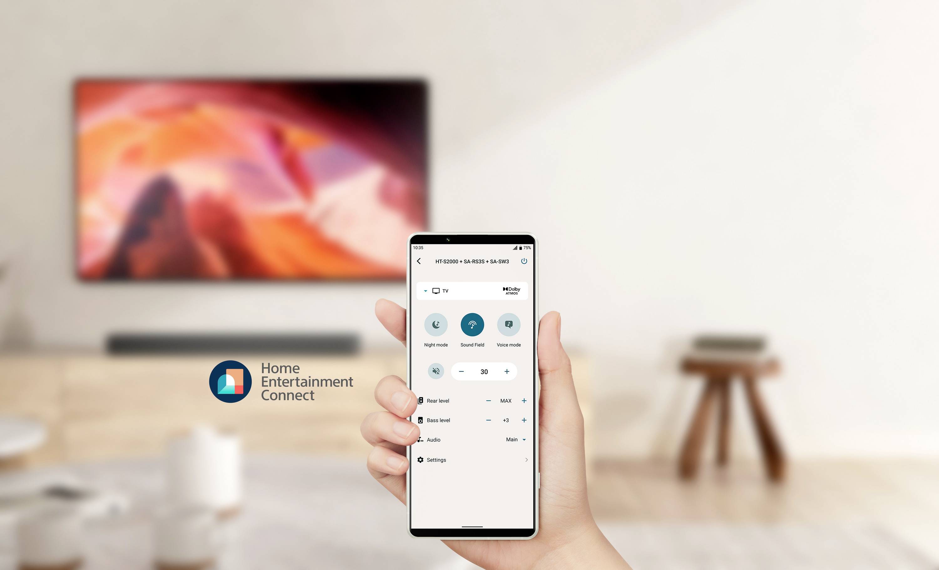 Uno smartphone mostra l'app 'Home Entertainment Connect' per il controllo di un televisore. Sullo sfondo, sfocato, un televisore acceso.