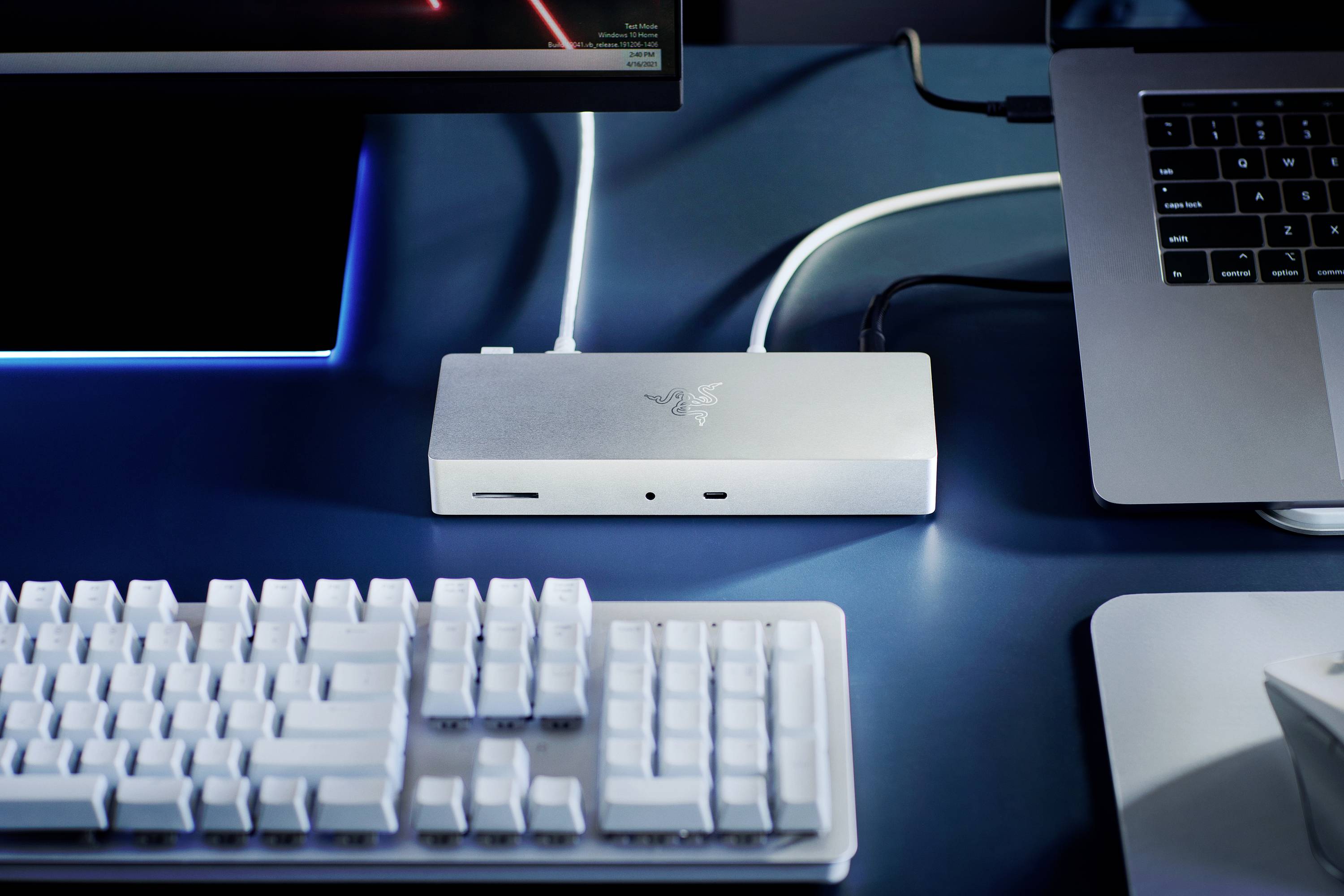 Un dock argentato collega un laptop a un monitor esterno e a una tastiera su una scrivania.