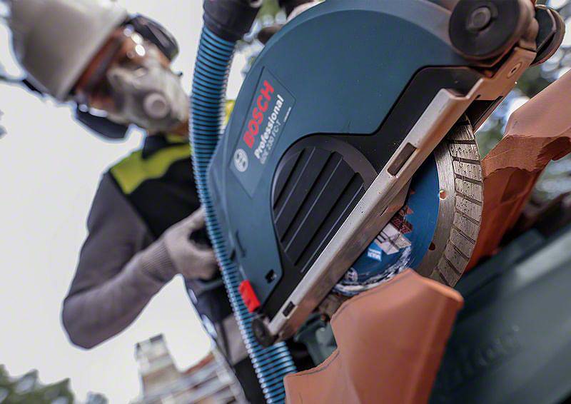 Lavoratore con mascherina protettiva utilizza una sega elettrica Bosch per tagliare un mattone. La messa a fuoco è sulla lama della sega.