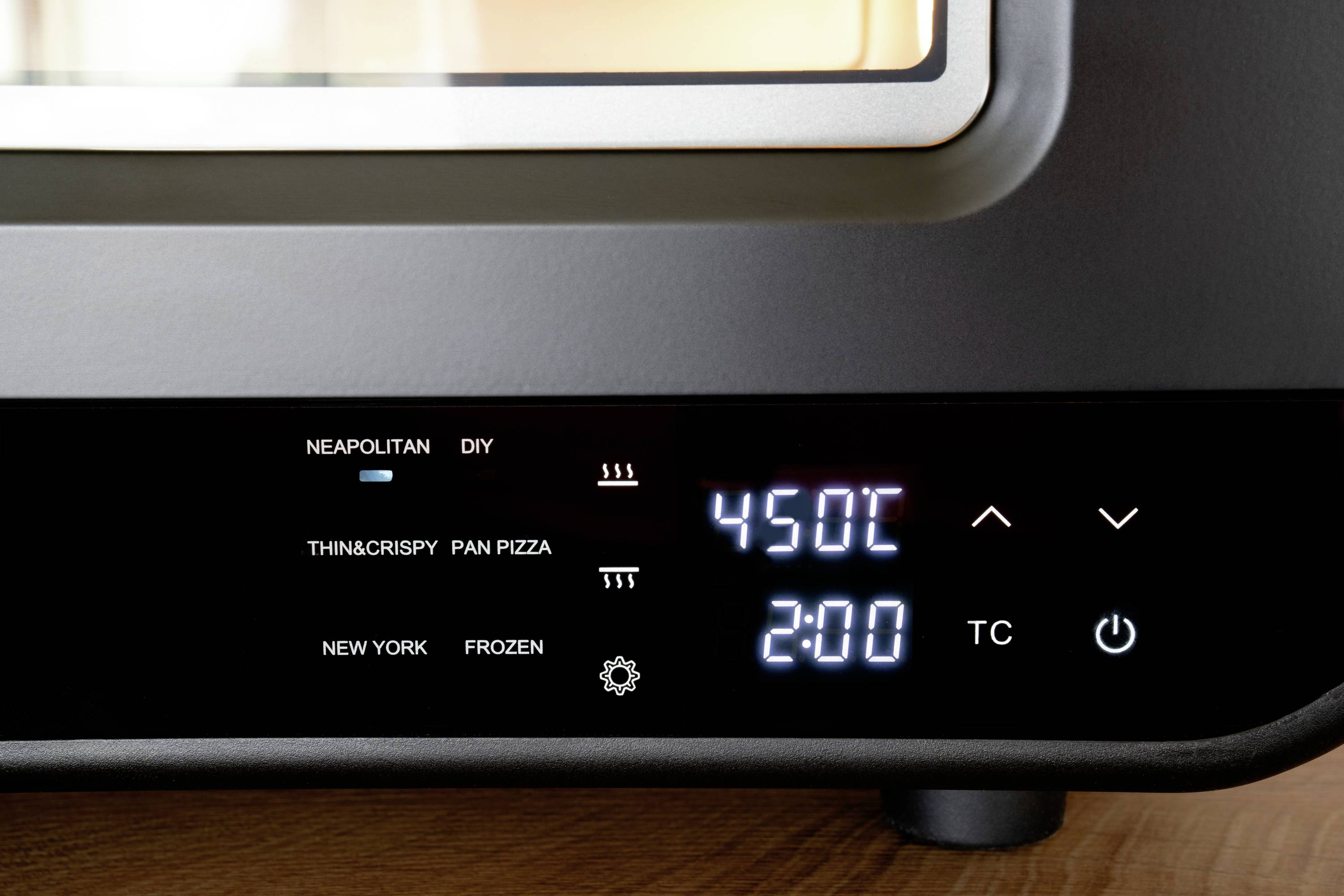 Un display del forno mostra le seguenti impostazioni: 'Napoletana', 'Fai da te', 'Croccante e sottile', 'Pizza in teglia', 'New York', 'Surgelata'. Temperatura 450°C, tempo 2:00 ore.