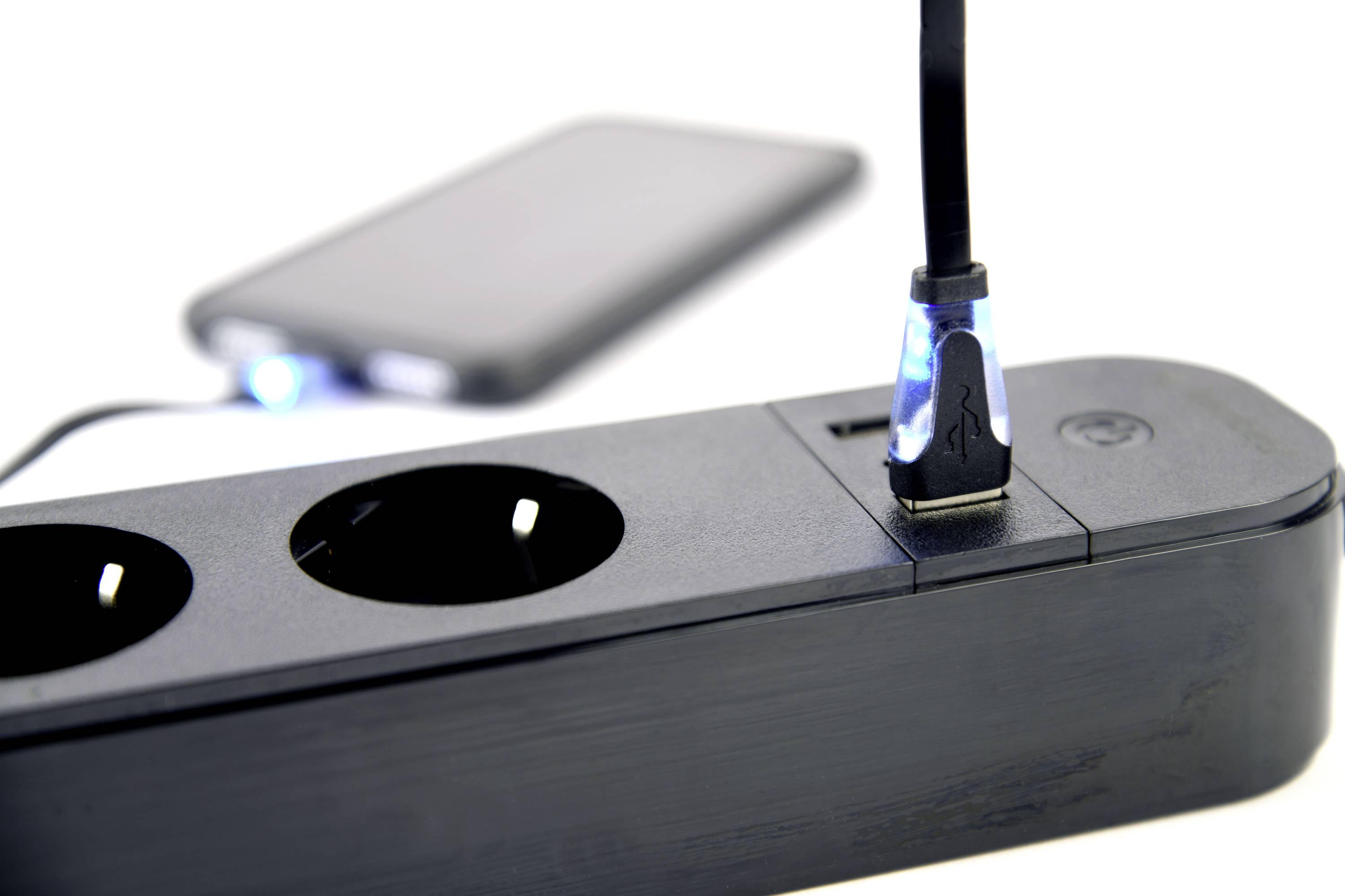 Multipresa nera con porta USB; un cavo USB è collegato e sta caricando uno smartphone sullo sfondo.